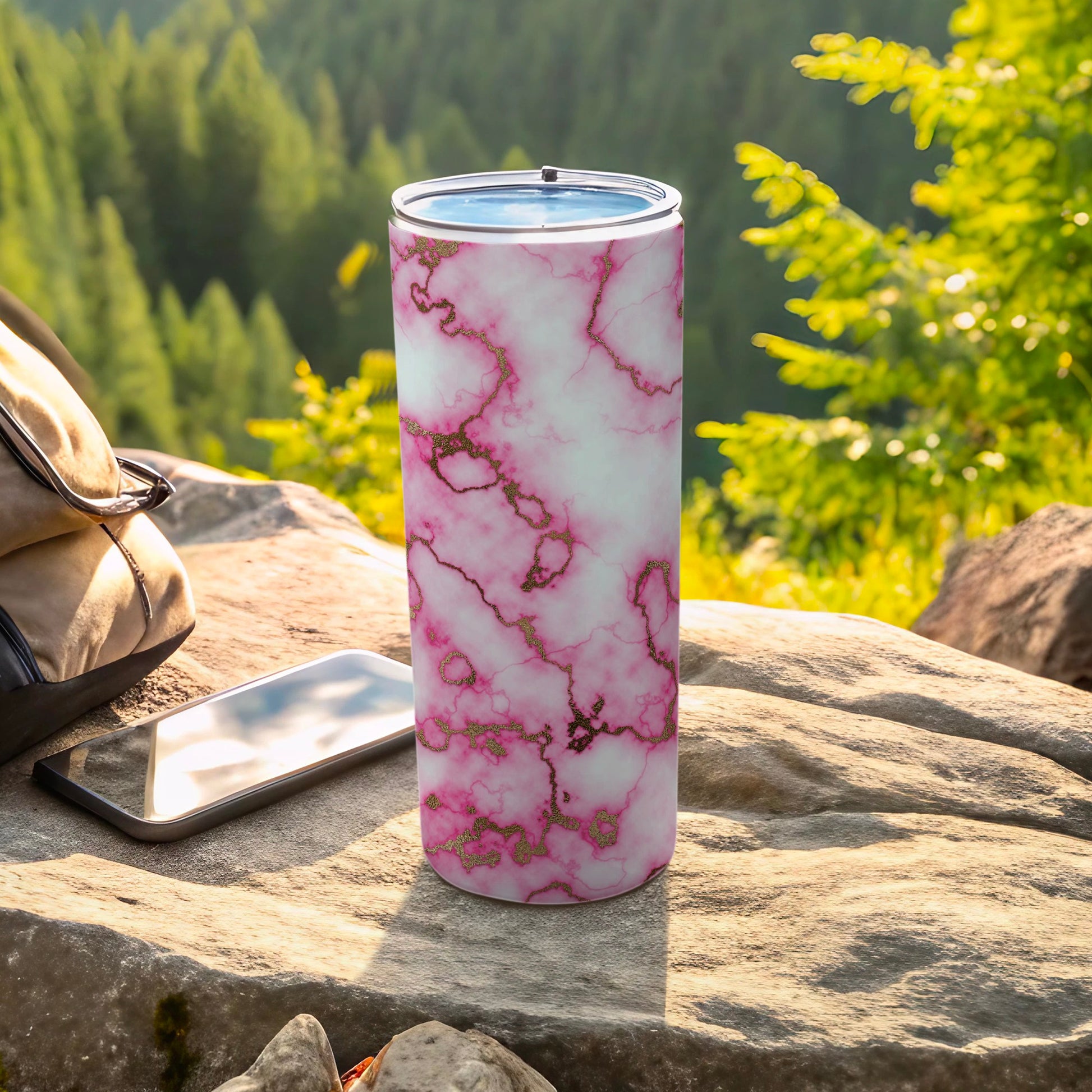 Tall tumbler with pink and gold marble pattern on rocky surface.