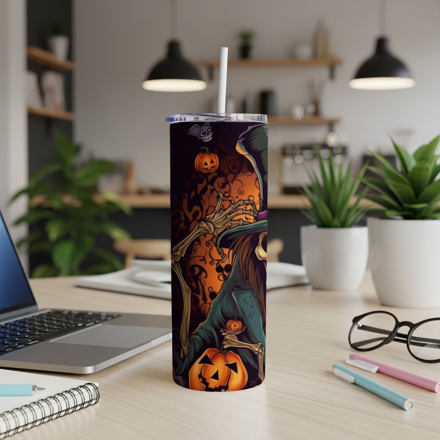 Halloween tumbler with skeleton witch and pumpkins on a desk.