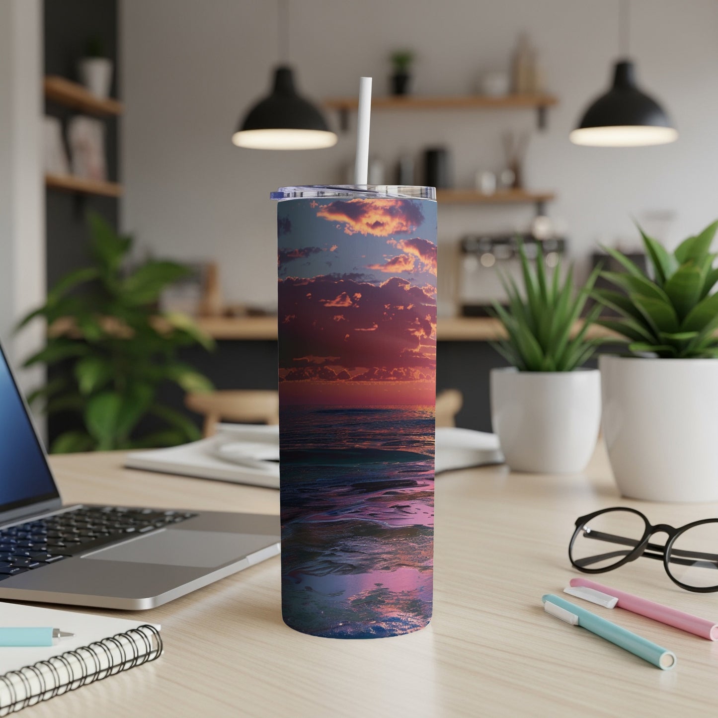 Ocean sunset depicted on a white tumbler with straw on a desk.