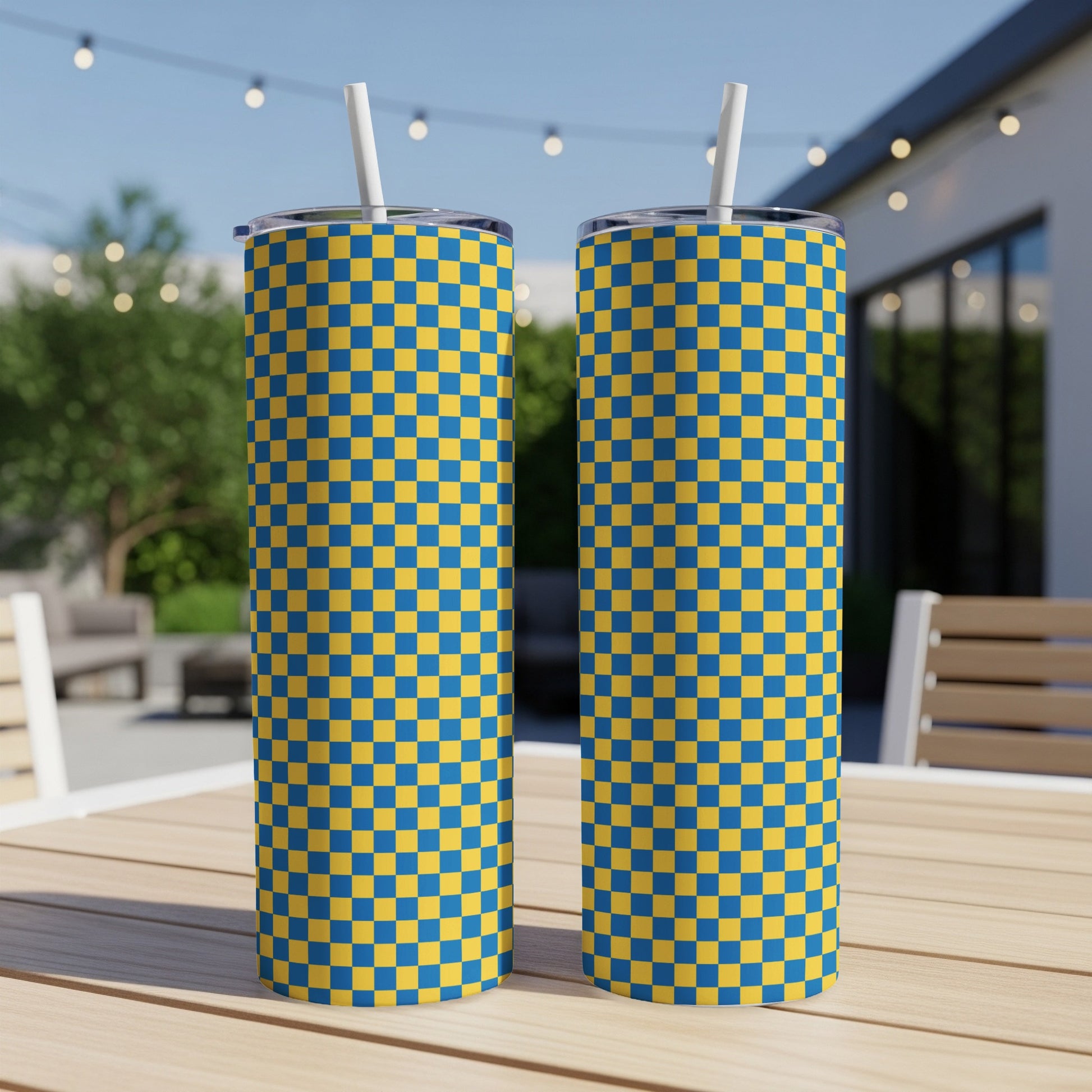 Two blue and yellow checkered tumblers on a wooden table outdoors.