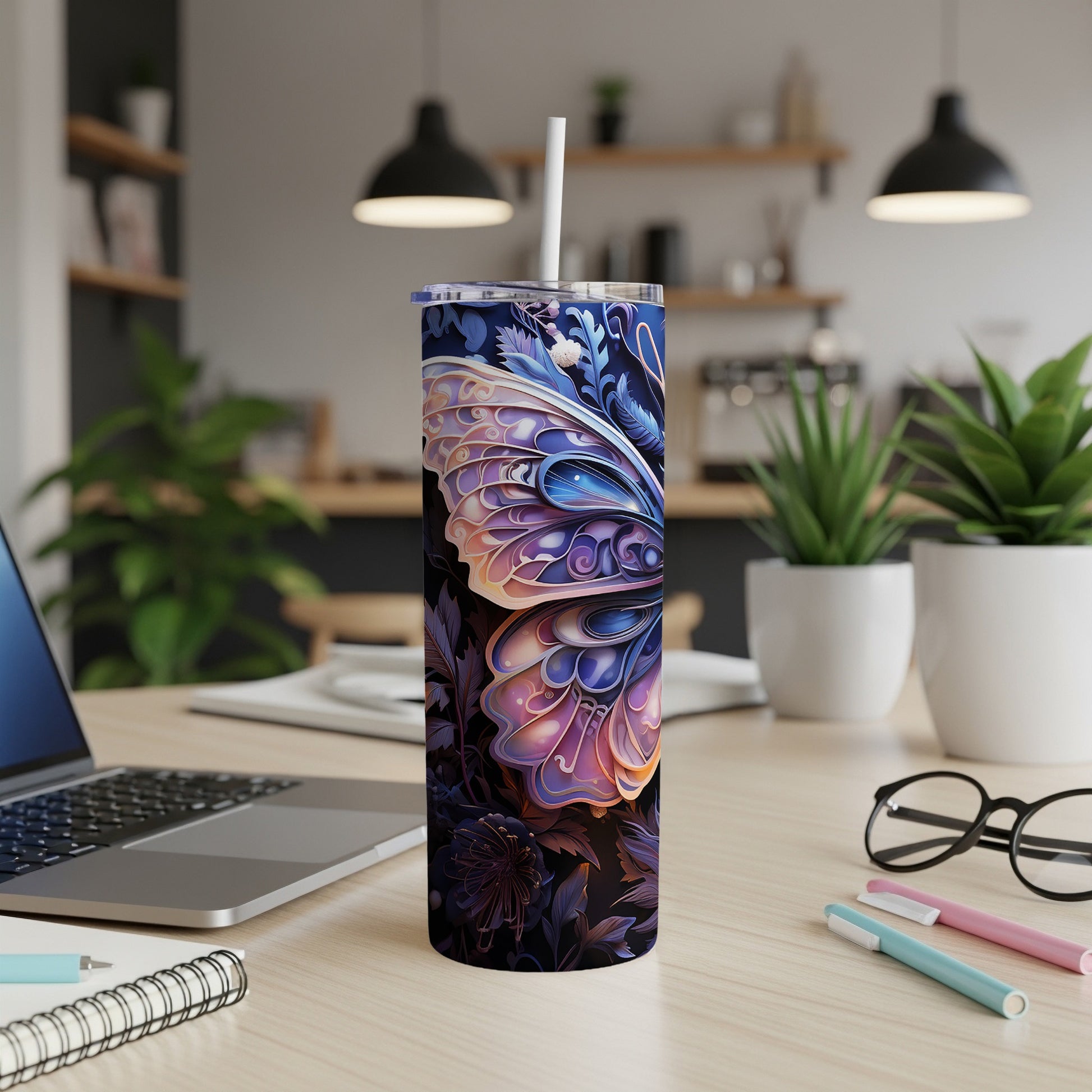 Blue butterfly tumbler with straw on desk, next to laptop and pens.
