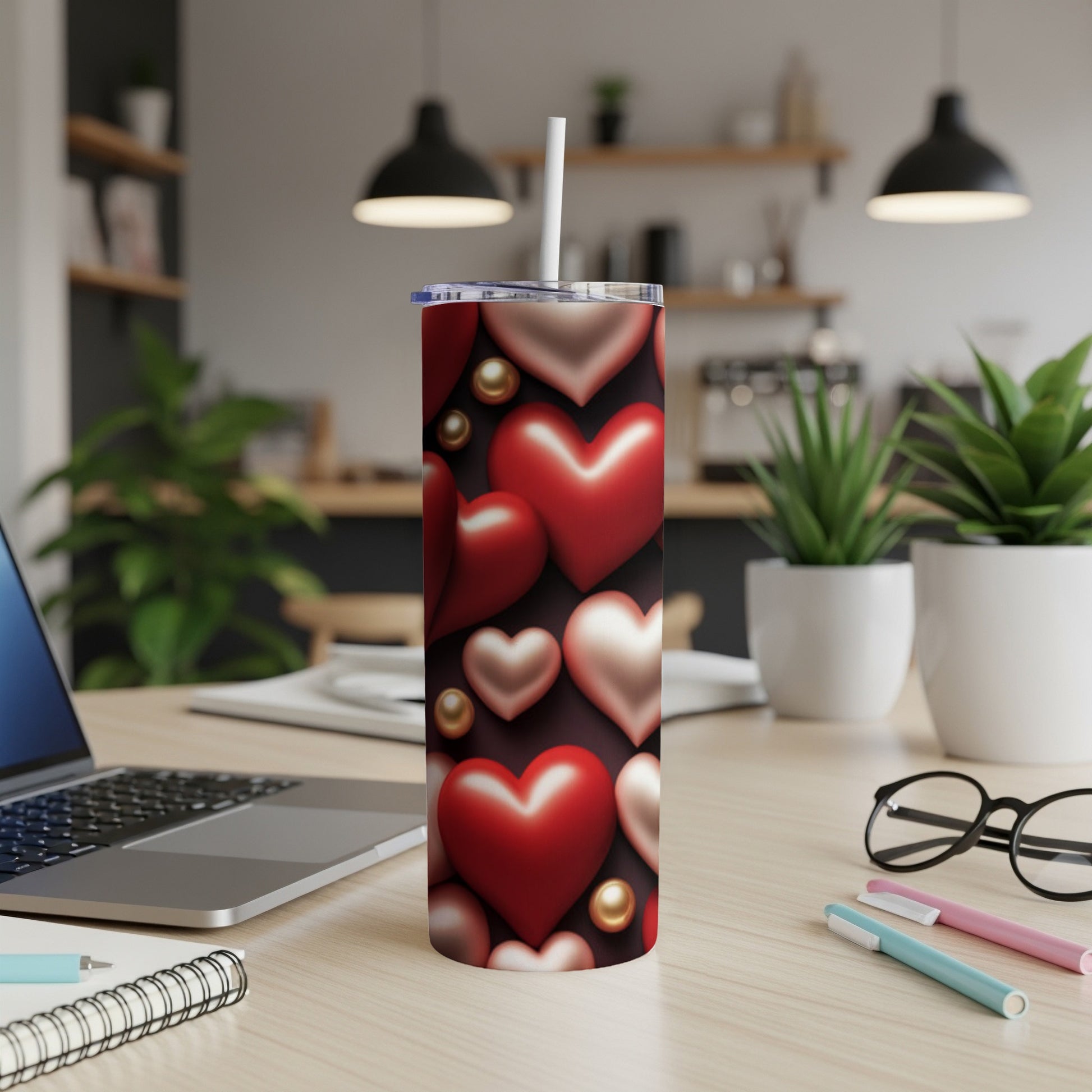 Red and pink heart-patterned tumbler with straw on a desk.