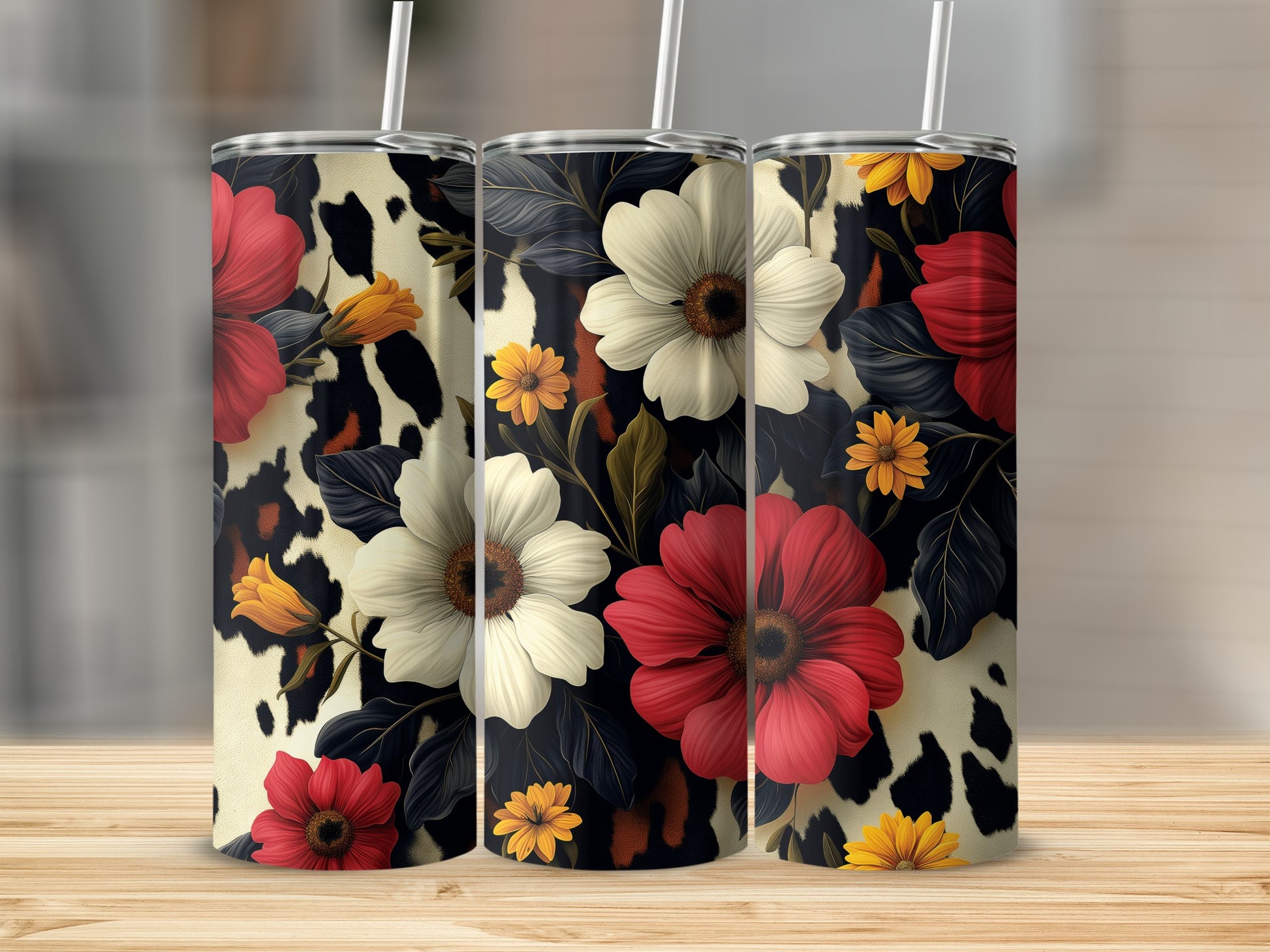 Three tumblers with floral and cow print designs stand on a wooden surface.