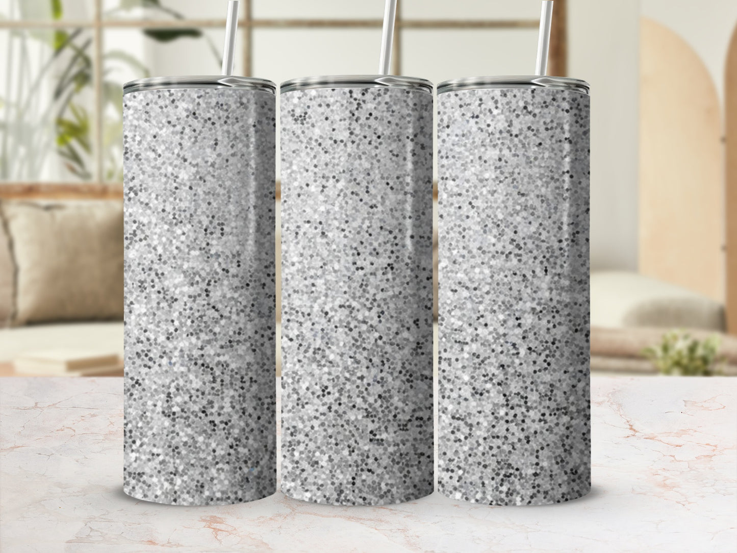 Three silver glitter tumblers with straws on a marble surface.