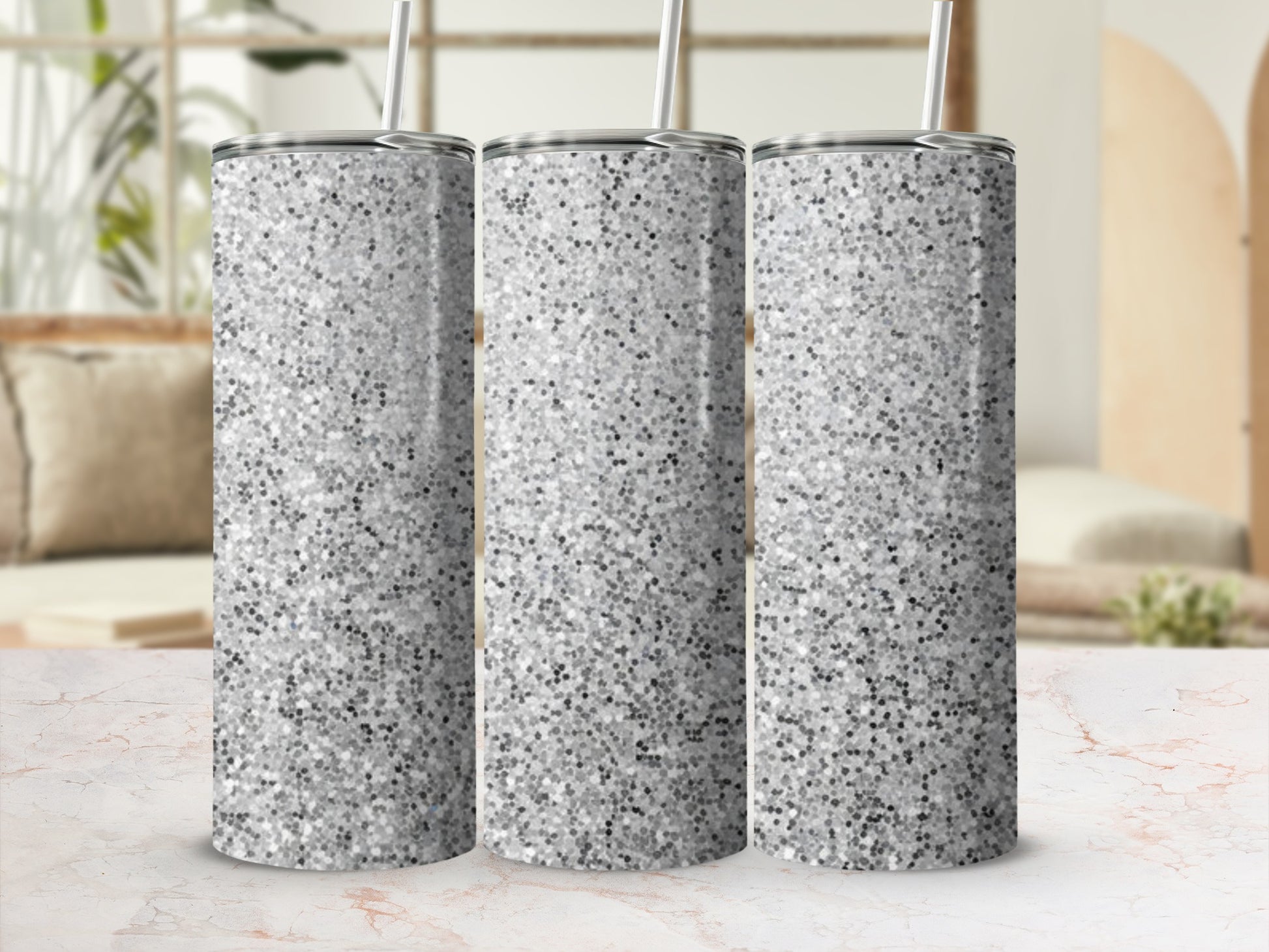 Three silver glitter tumblers with straws on a marble surface.