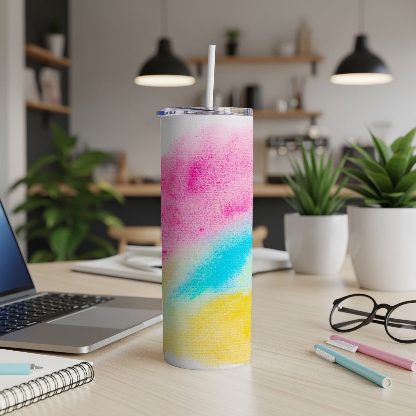 Tumbler with colorful watercolor design, straw, laptop, and pens on desk.