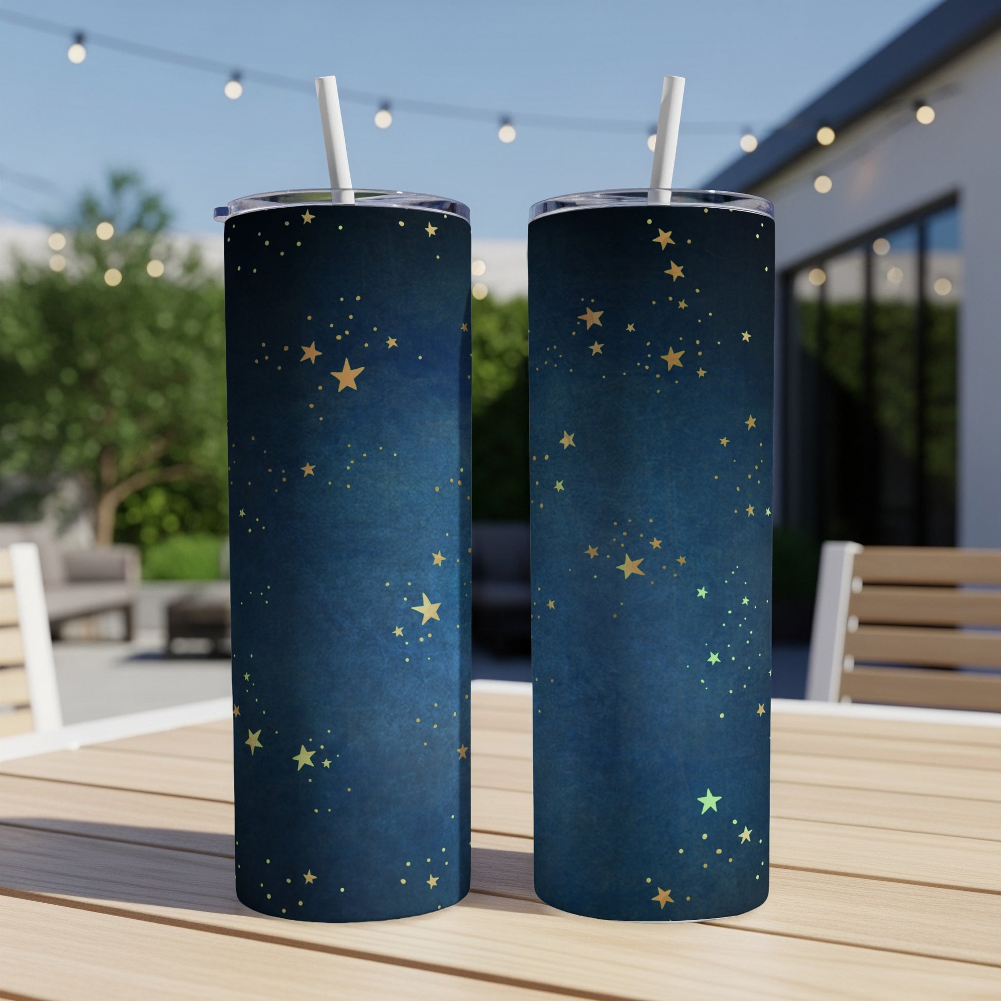 Two dark blue tumblers with gold star patterns and white straws, displayed on a wooden table.