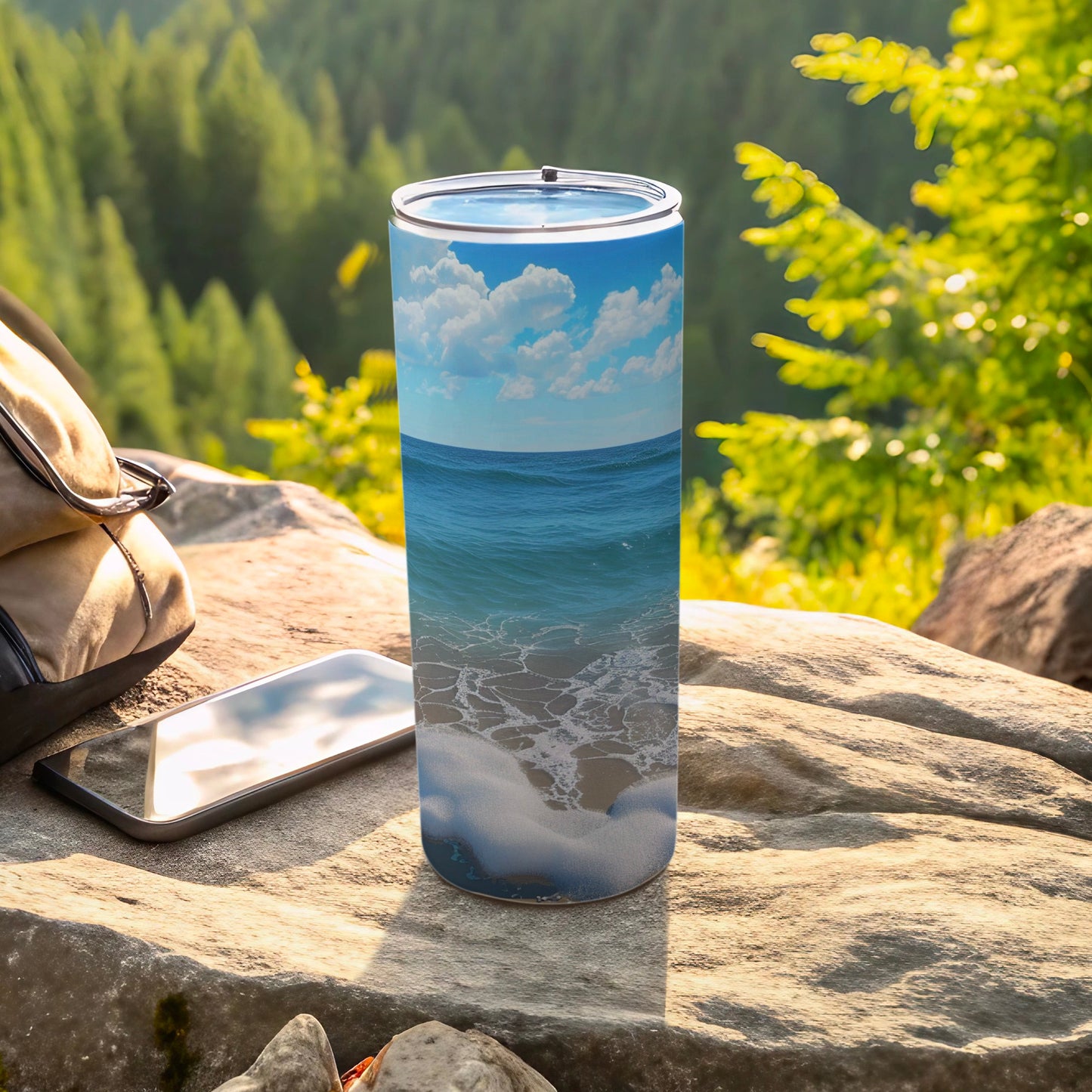 Ocean waves and beach scene on a tall tumbler beside a backpack and phone.