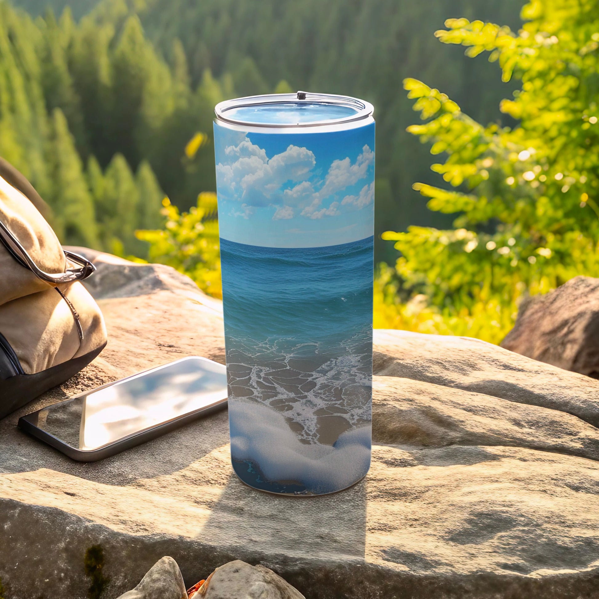 Ocean waves and beach scene on a tall tumbler beside a backpack and phone.