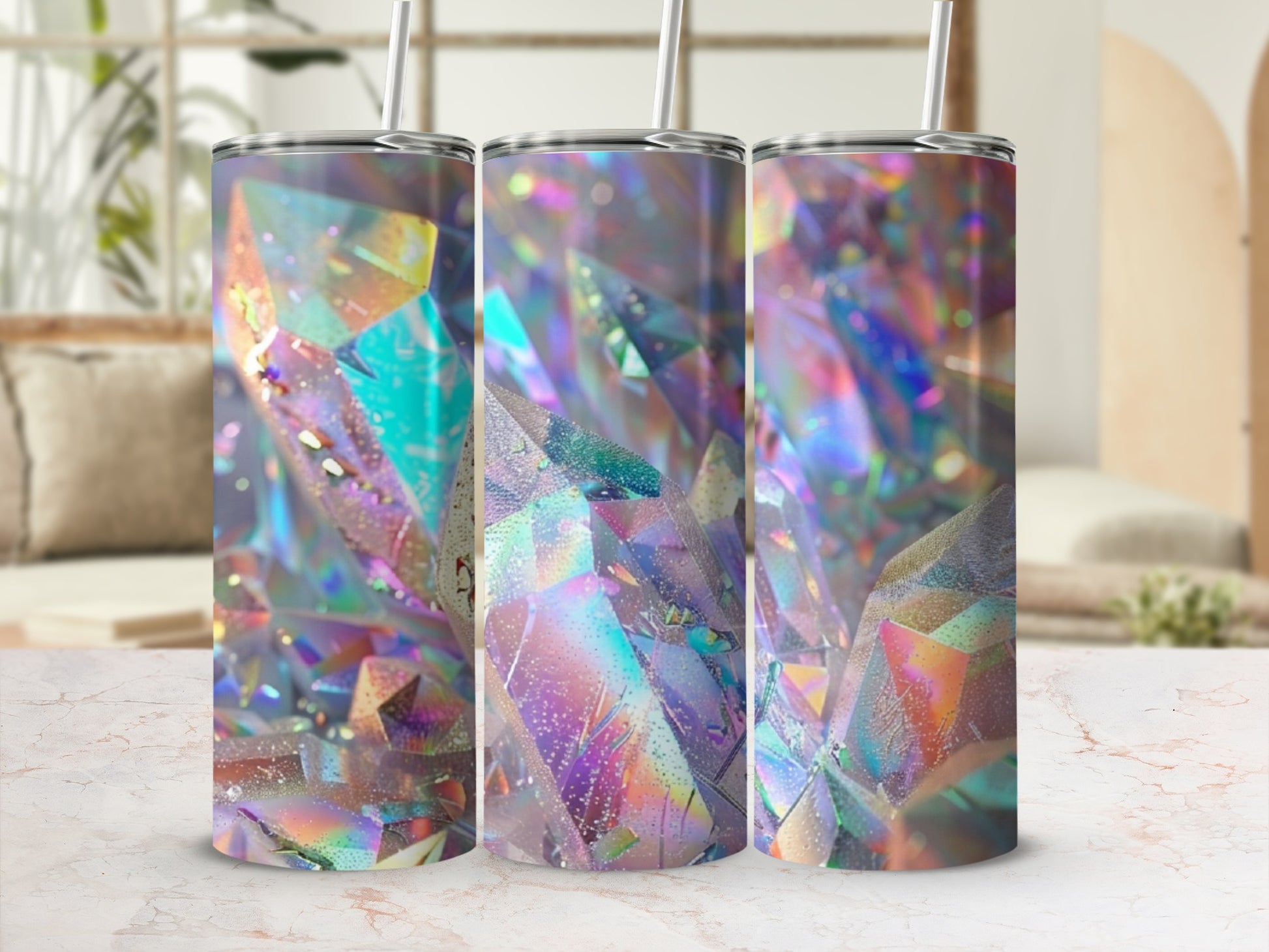 Three tumblers with iridescent crystal designs and straws on a marble surface.