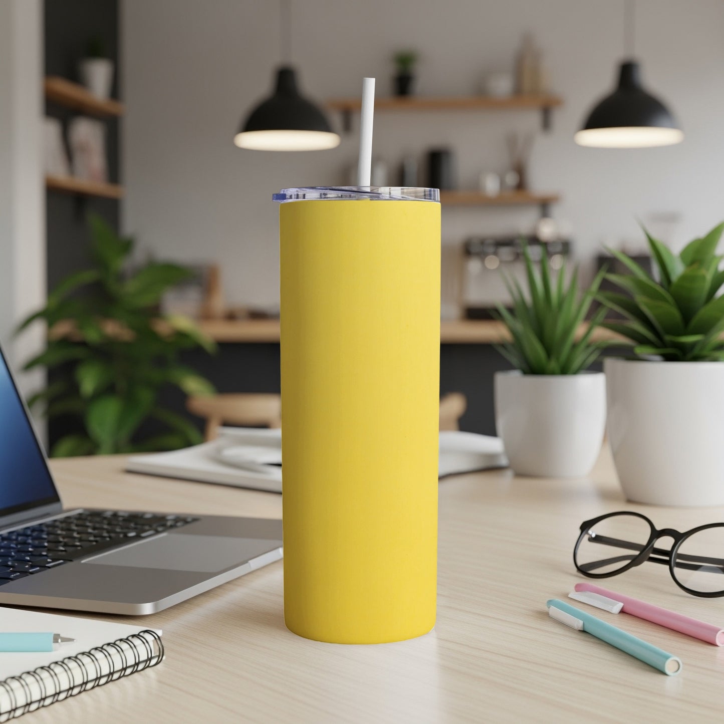 Yellow tumbler with a straw on a desk next to a laptop and pens.