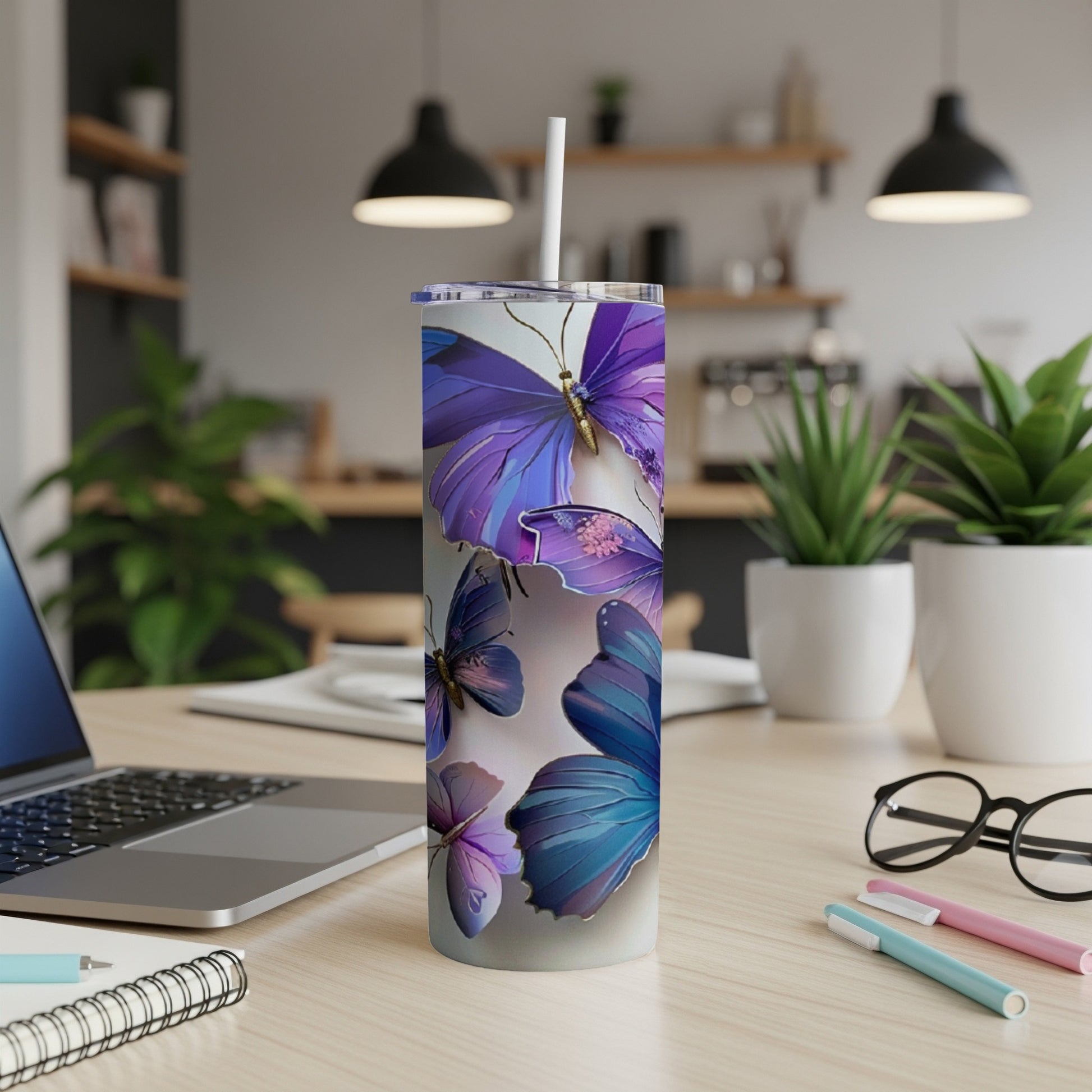 Tall tumbler with purple and blue butterflies on a desk with a laptop.
