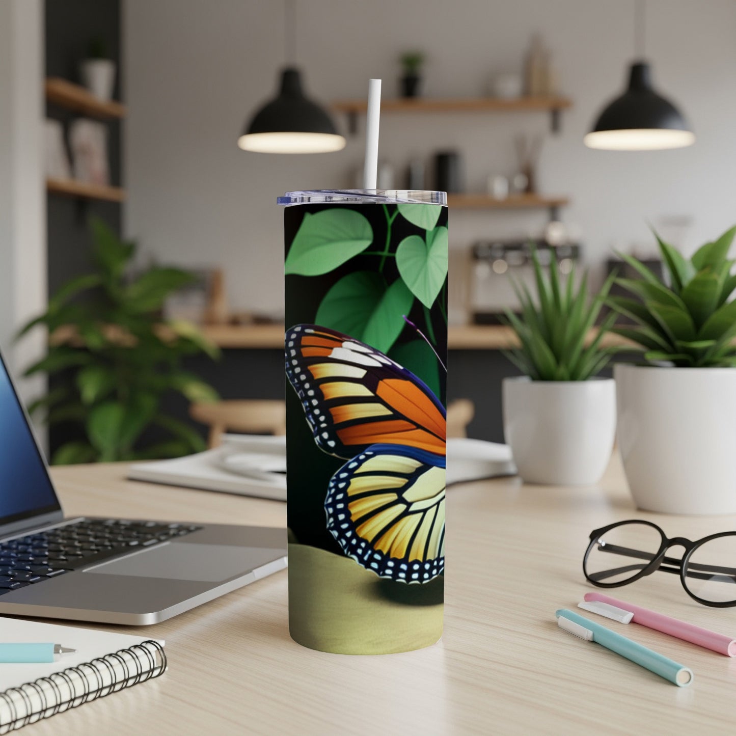 Tall tumbler with monarch butterfly art, straw, on a desk.