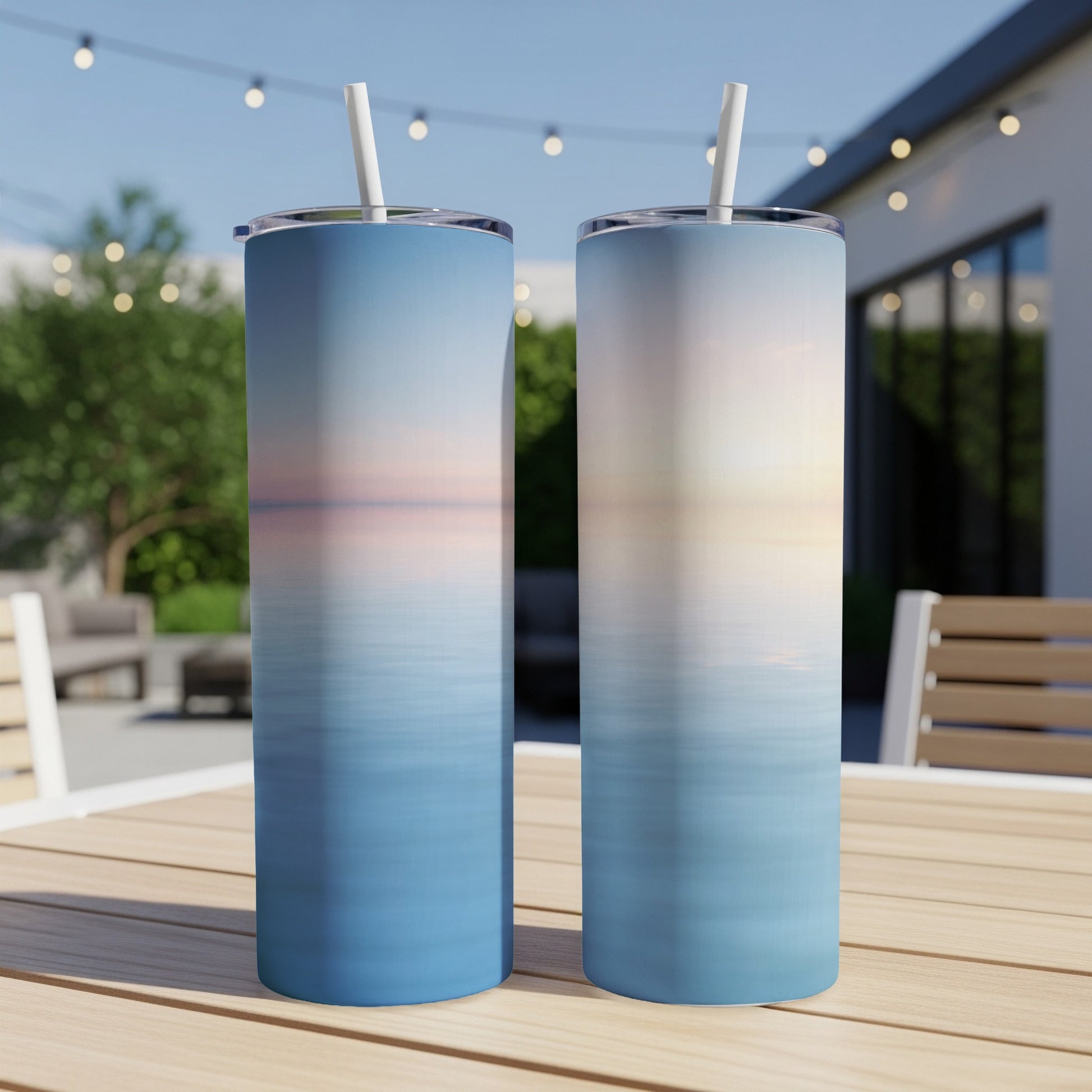 Two blue tumblers with sunset over water design sit on a wooden table.