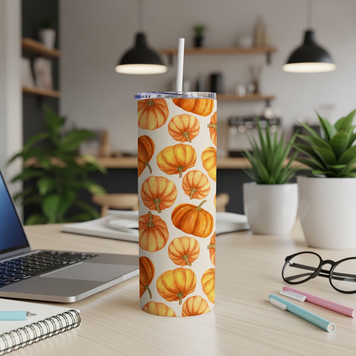 Pumpkin patterned tumbler with straw on a desk.