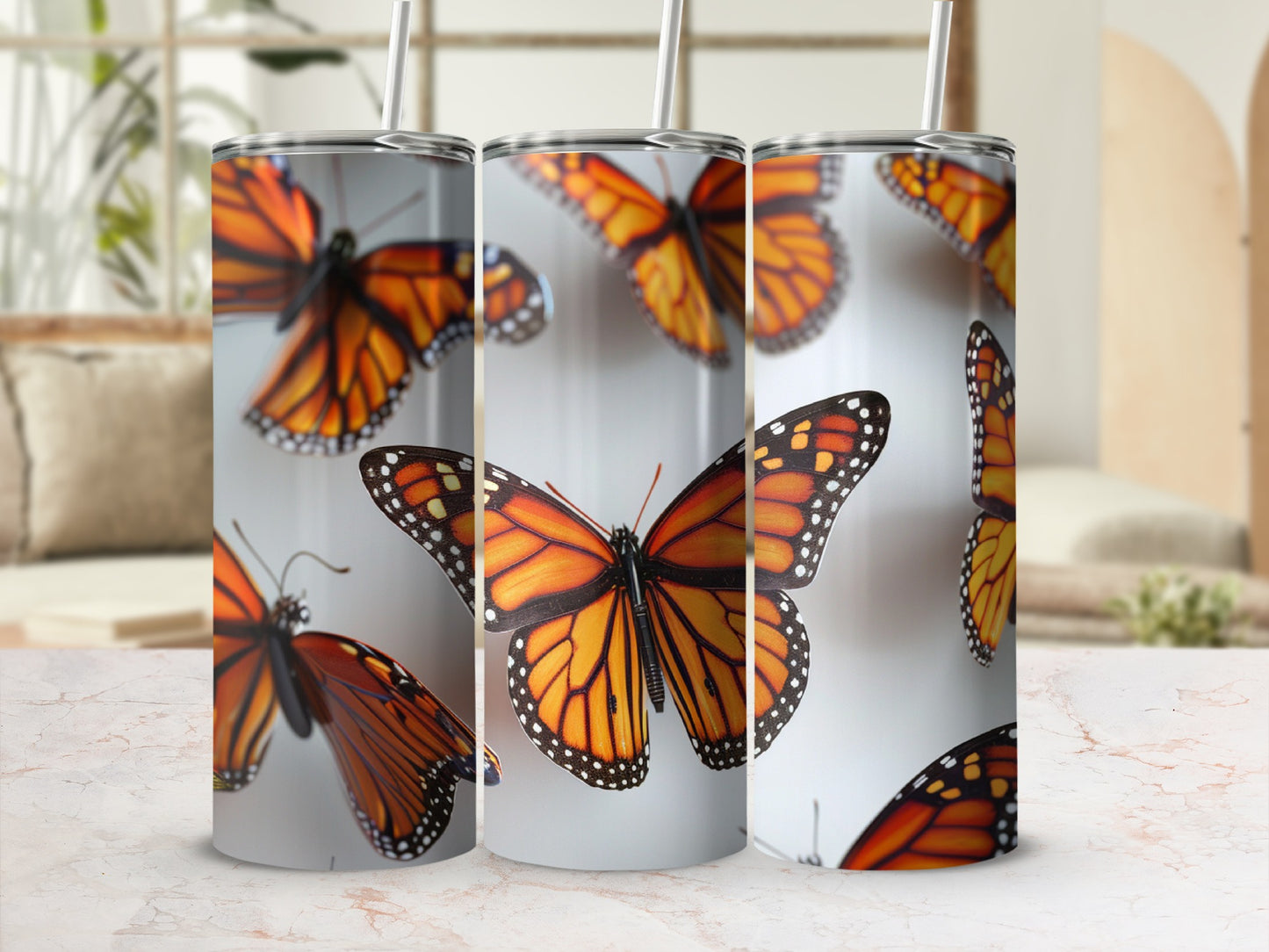 Three tumblers with monarch butterfly pattern arranged on a white and pink marble surface.
