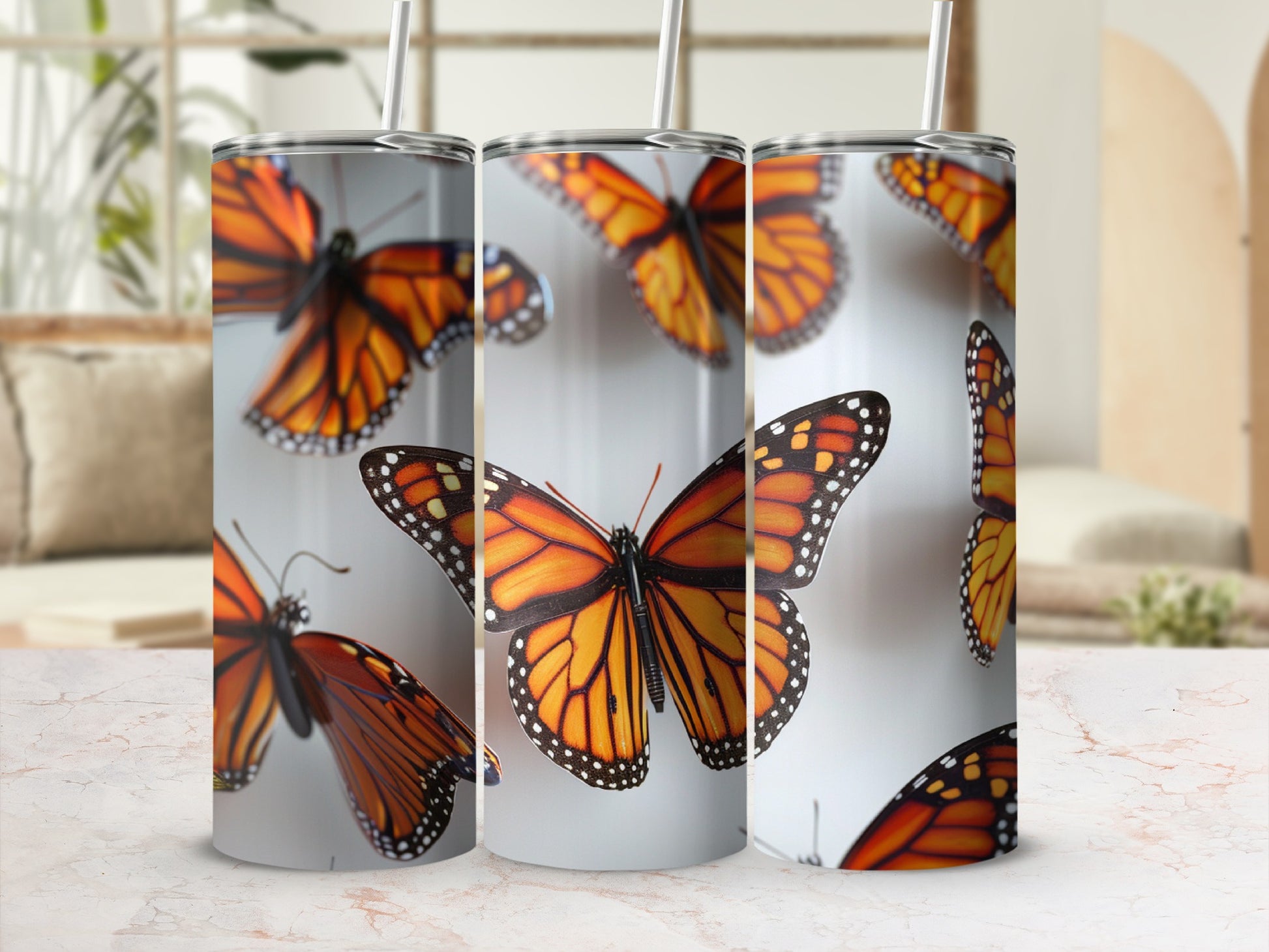 Three tumblers with monarch butterfly pattern arranged on a white and pink marble surface.