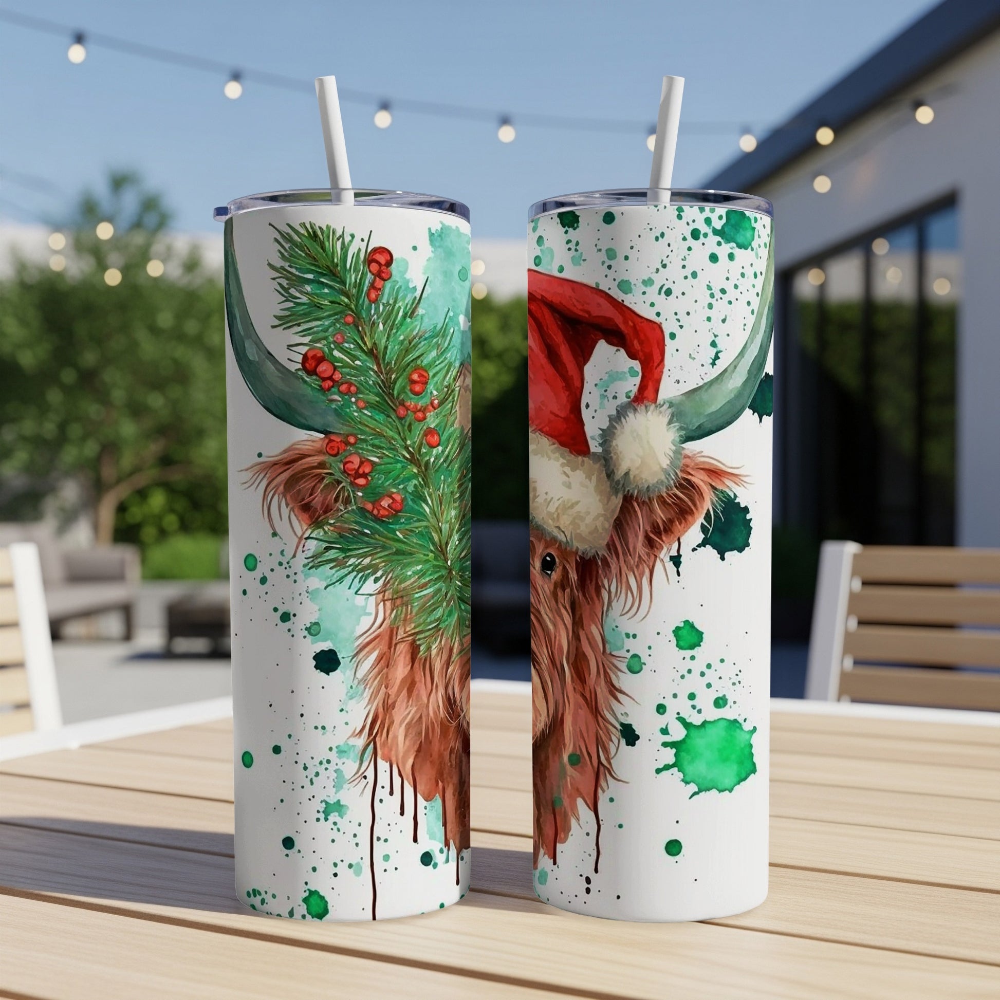 Two tumblers with a Highland cow wearing a Santa hat, adorned with pine sprigs.