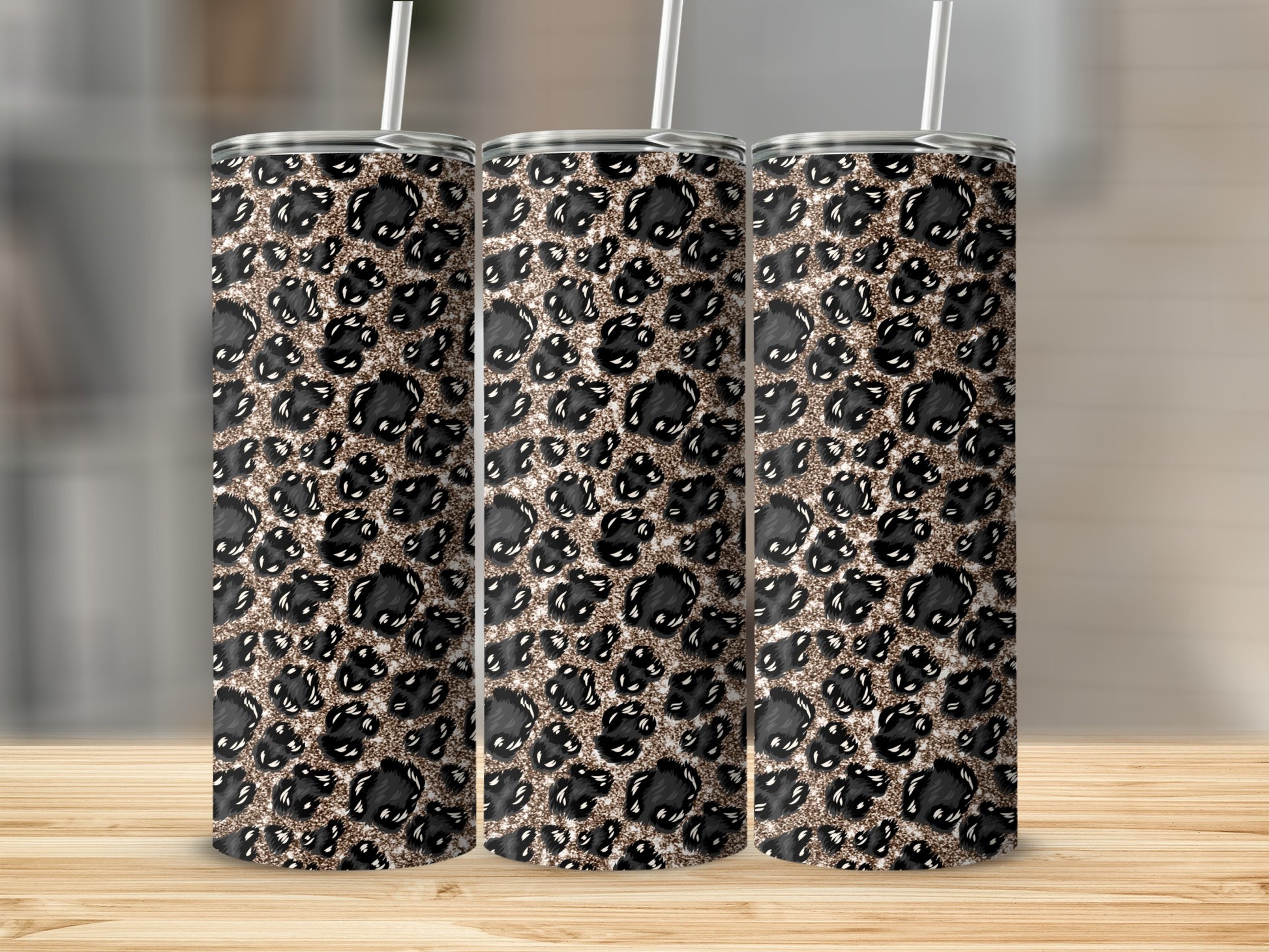 Three glitter leopard print tumblers with straws on a wooden surface.