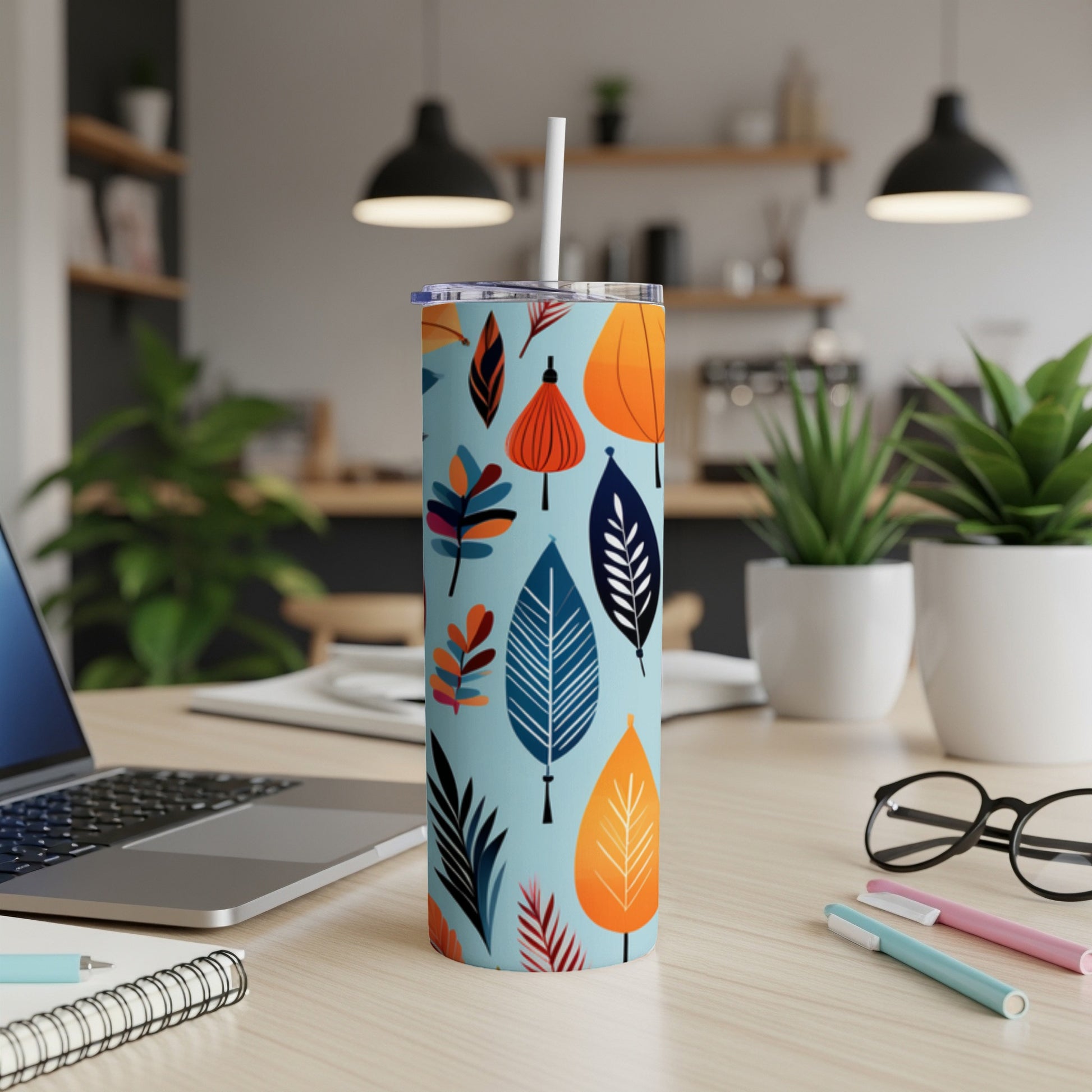 Blue tumbler with abstract colorful leaves pattern, on a desk with laptop and pens.