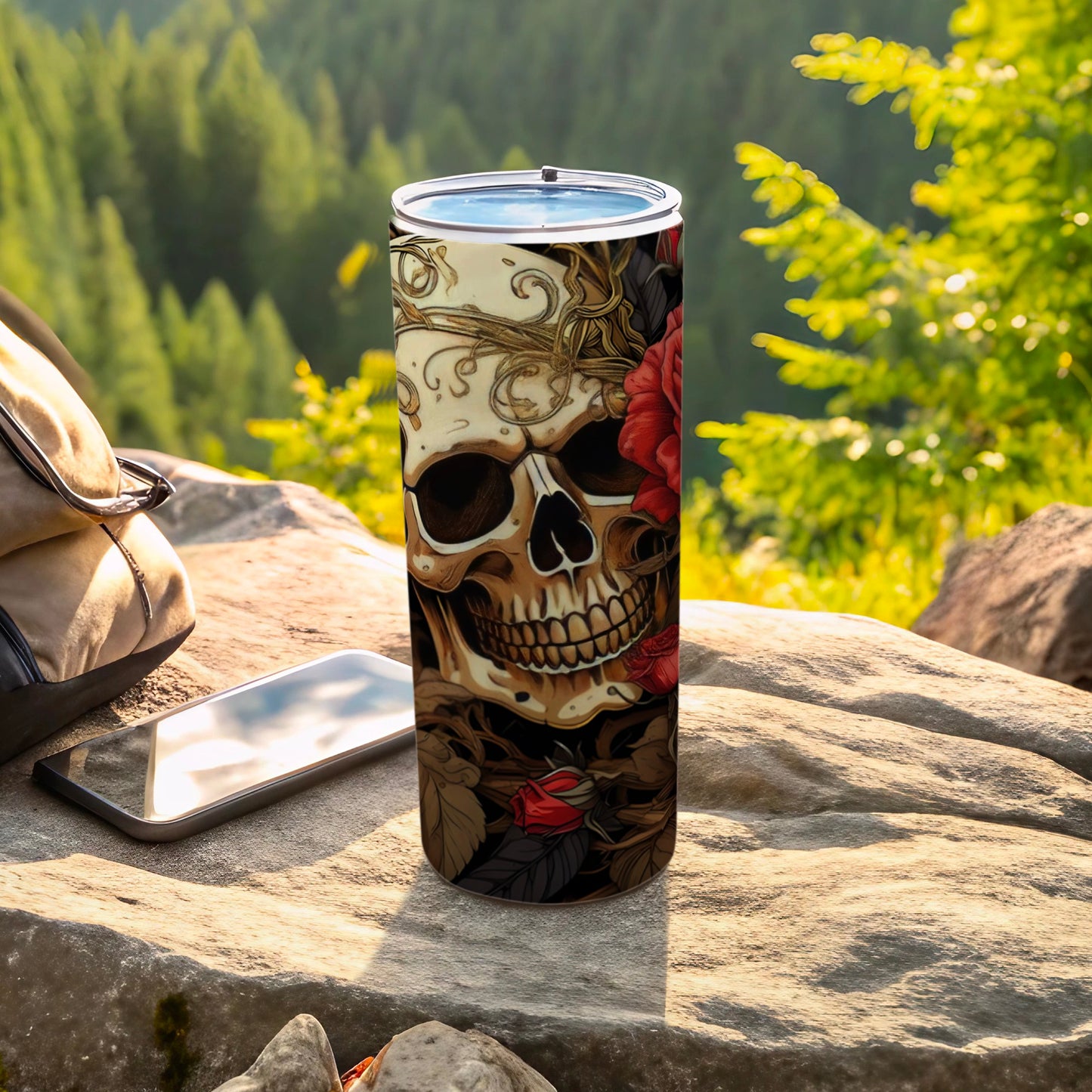 Tumbler with skull and rose design on outdoor rock surface.