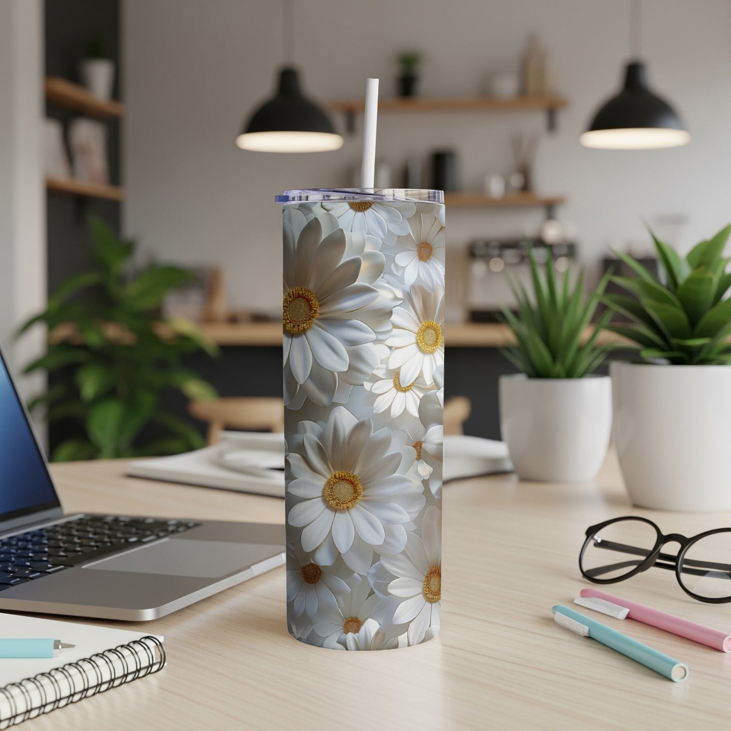 White daisies fill a tall, slim tumbler on a wooden desk.
