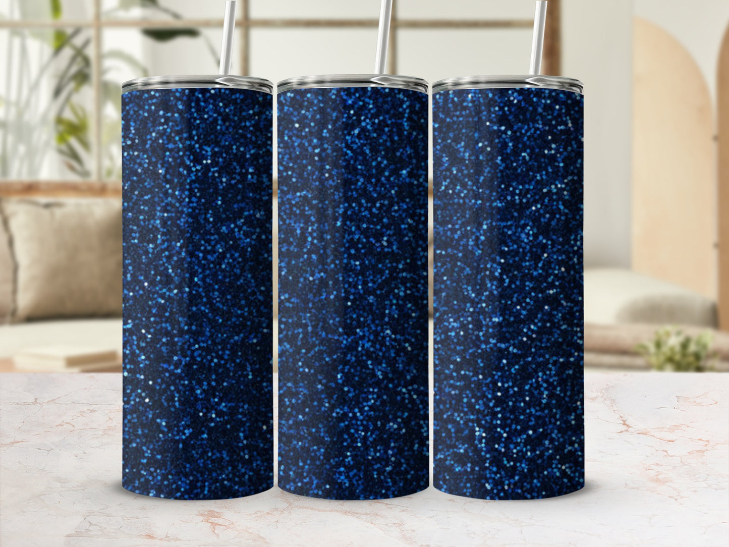 Three glittery dark blue tumblers with straws on a marble surface.