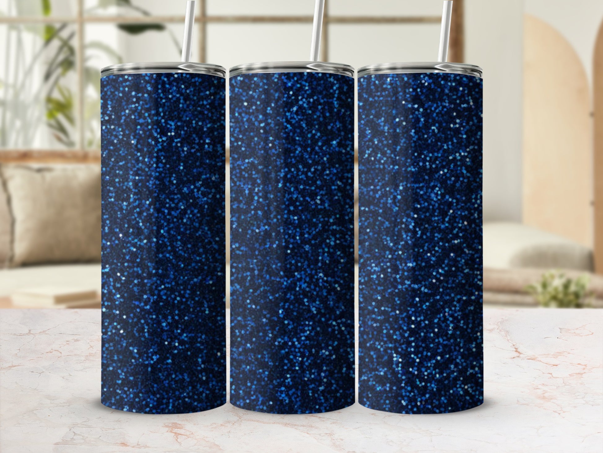 Three glittery dark blue tumblers with straws on a marble surface.