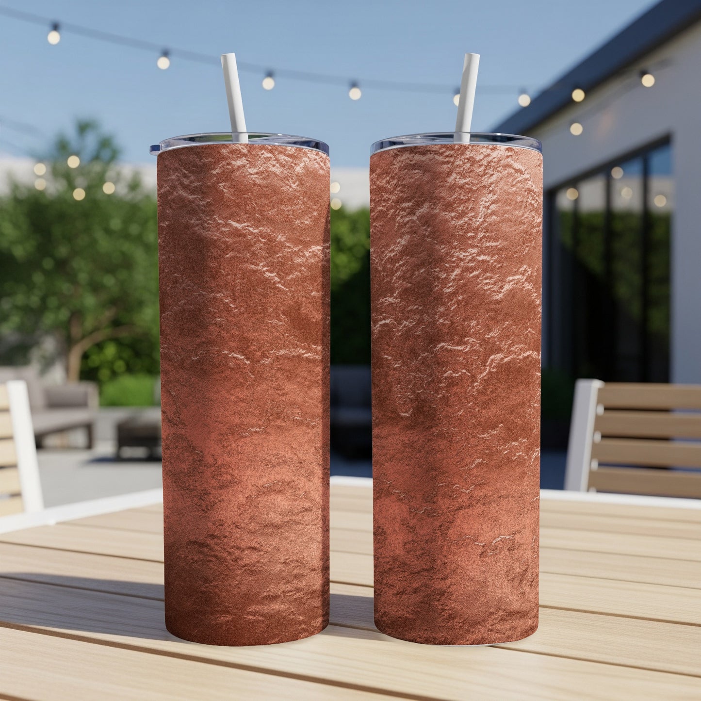 Two tall tumblers with textured rose gold finish and white straws on wooden table.