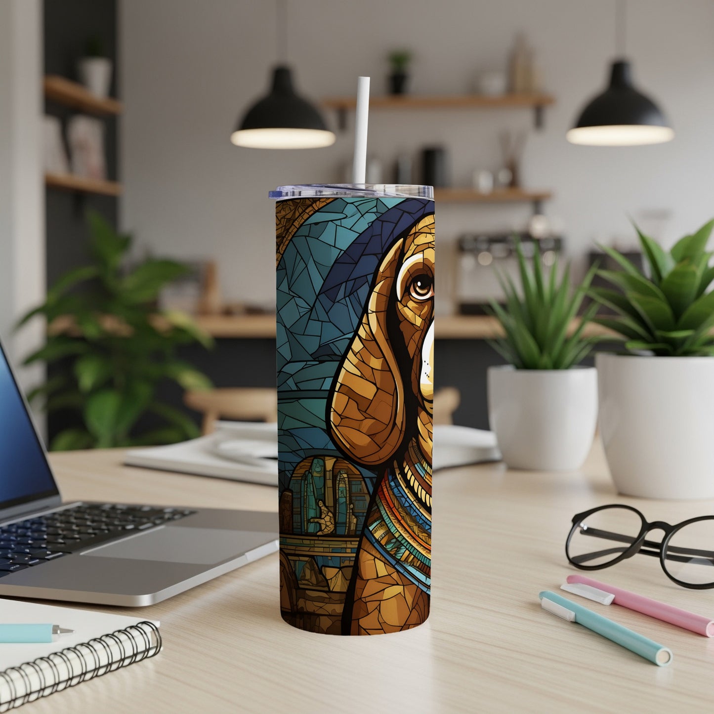 Tumbler with stained glass dog art and straw on a desk with laptop and notebooks.