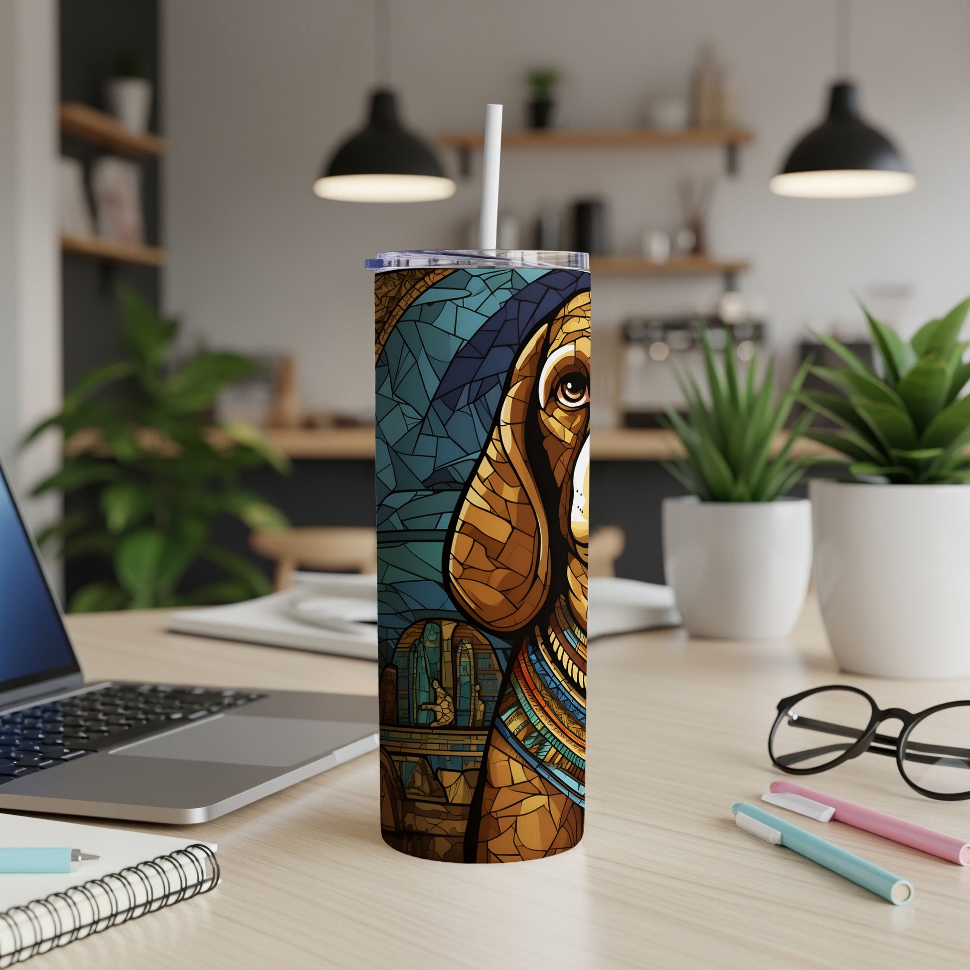 Tumbler with stained glass dog art and straw on a desk with laptop and notebooks.