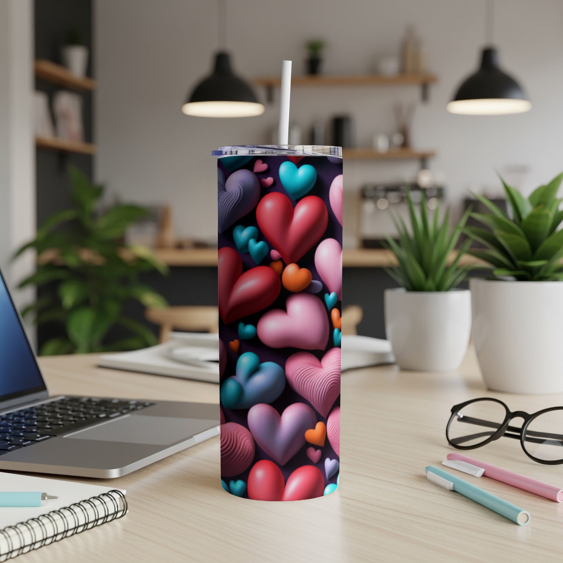 Tall tumbler with a colorful heart pattern, with a laptop and pens.