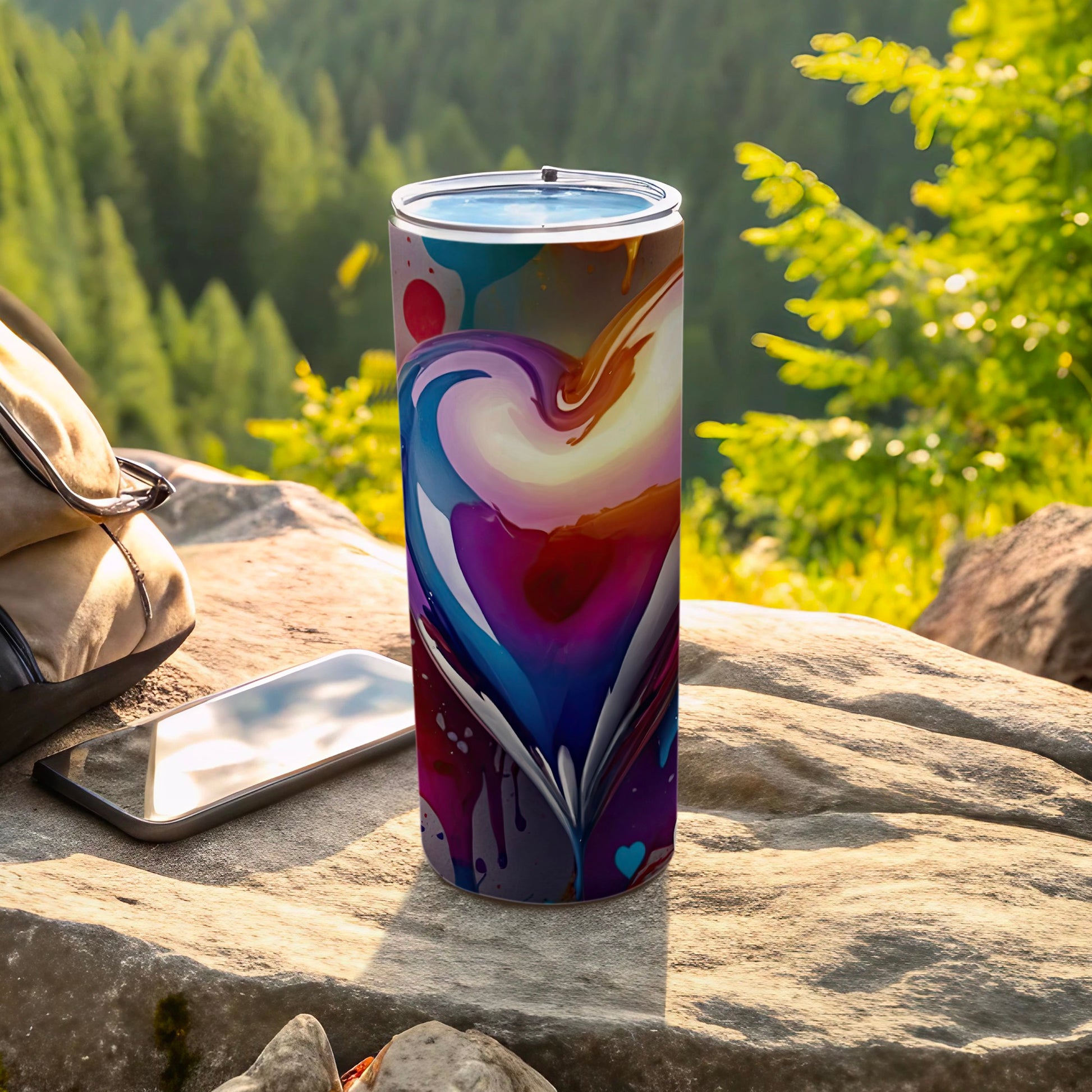 Tall tumbler with abstract heart design, phone, and backpack in outdoor setting.
