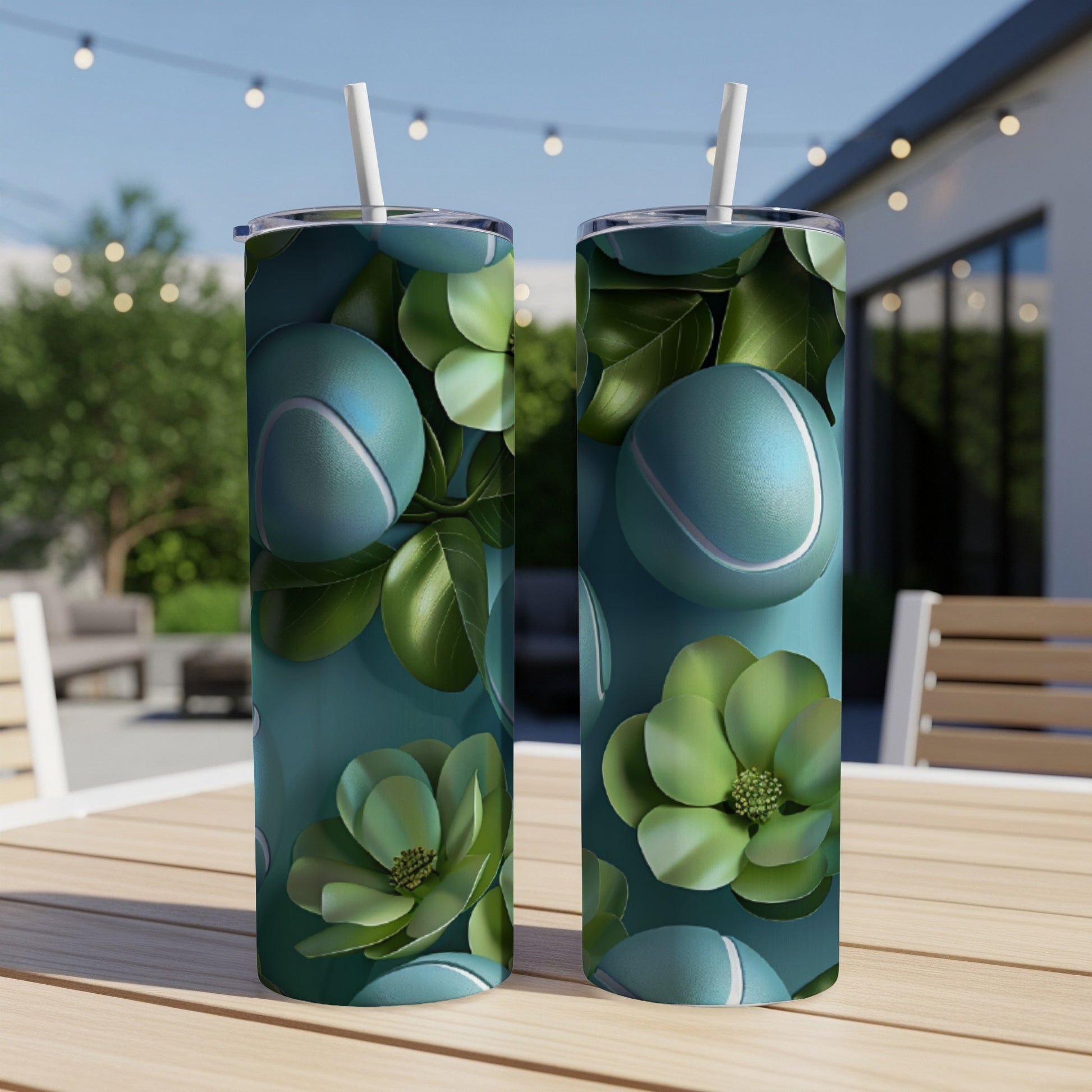 Two teal tumblers with tennis balls and green leaves pattern on a table.