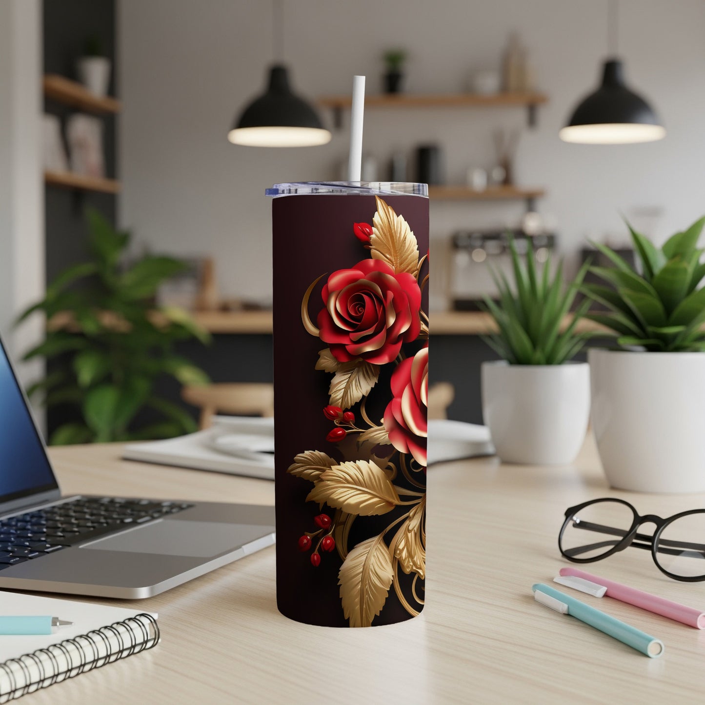 Maroon tumbler with red roses and gold leaves, on a desk.