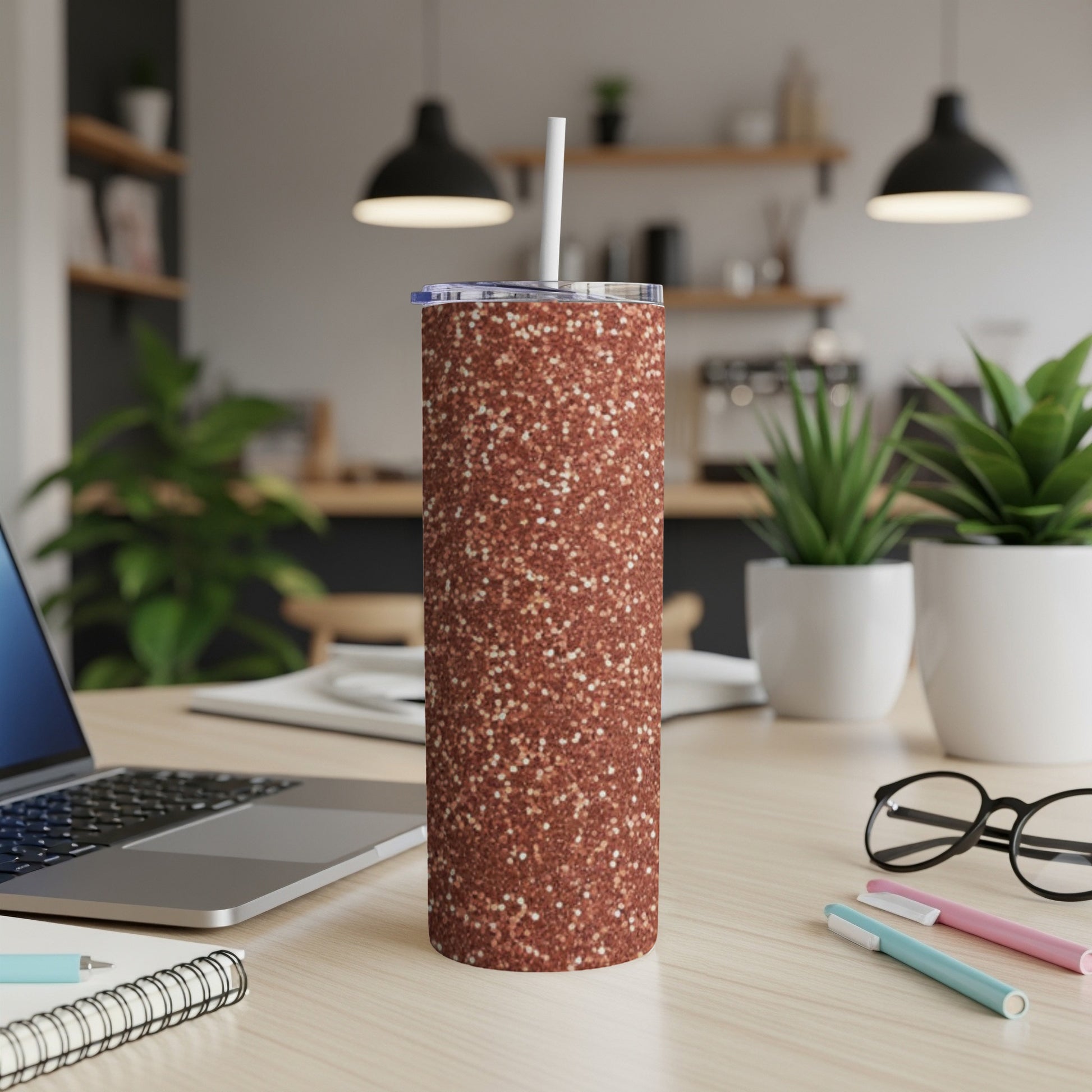 Glitter tumbler with straw on a desk next to a laptop.