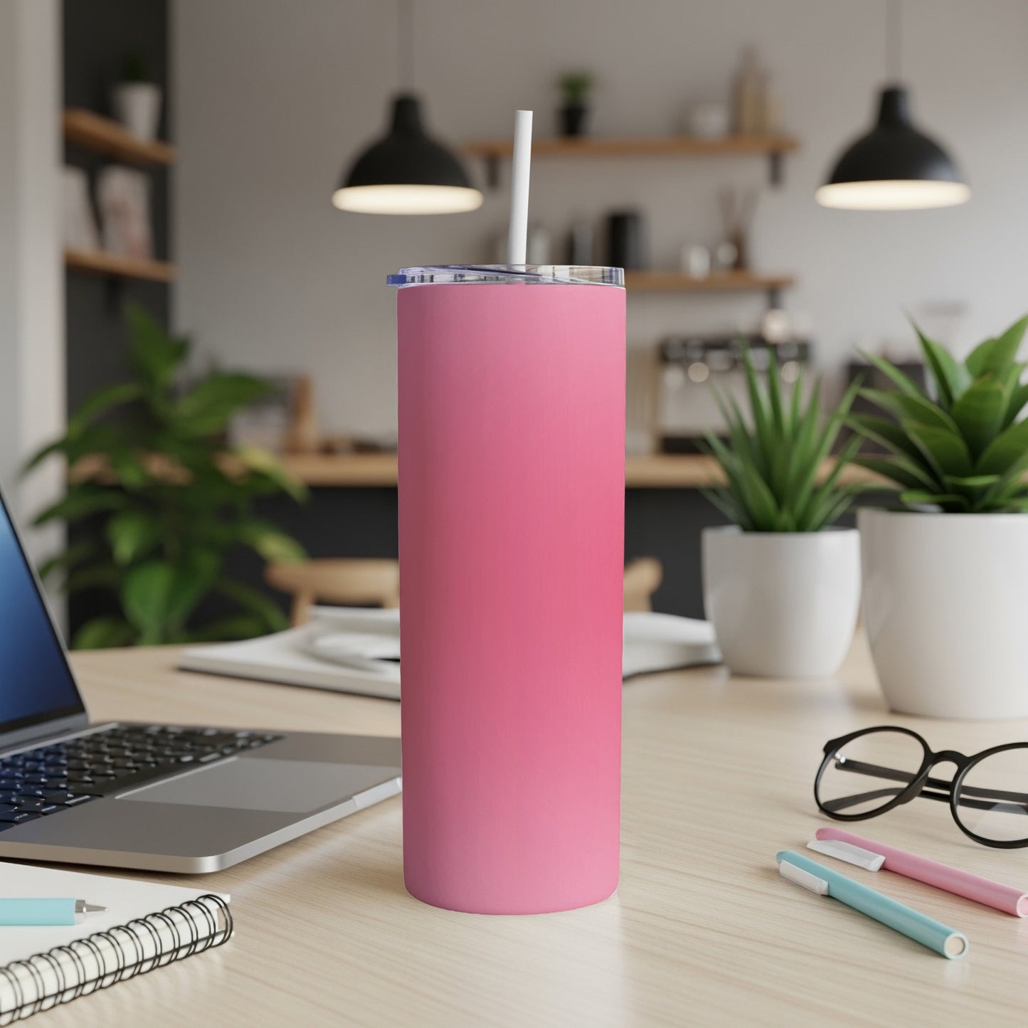 Pink tumbler with straw on a desk next to a laptop and plants.