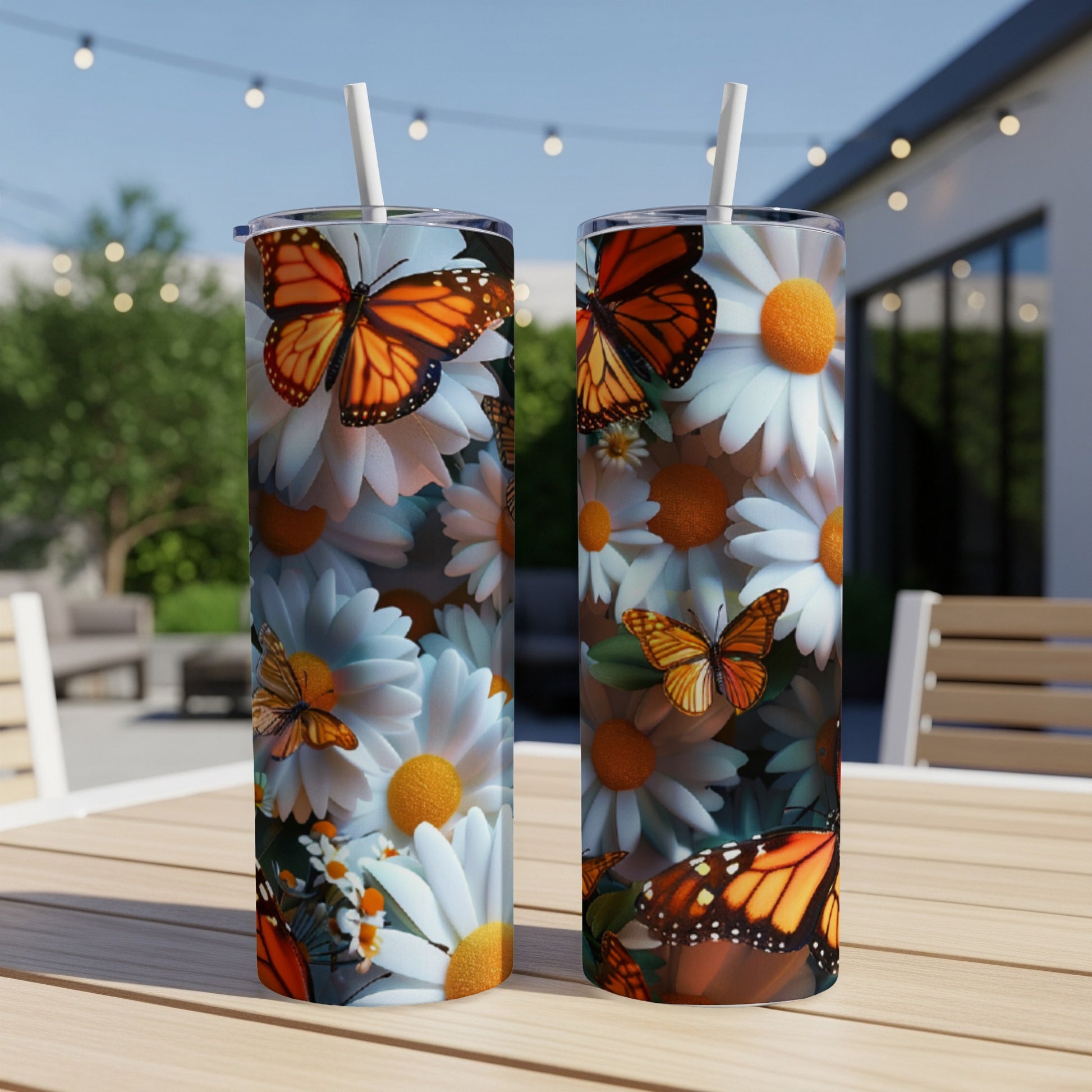 Two tumblers with butterflies and daisies, set on a wooden table outdoors.