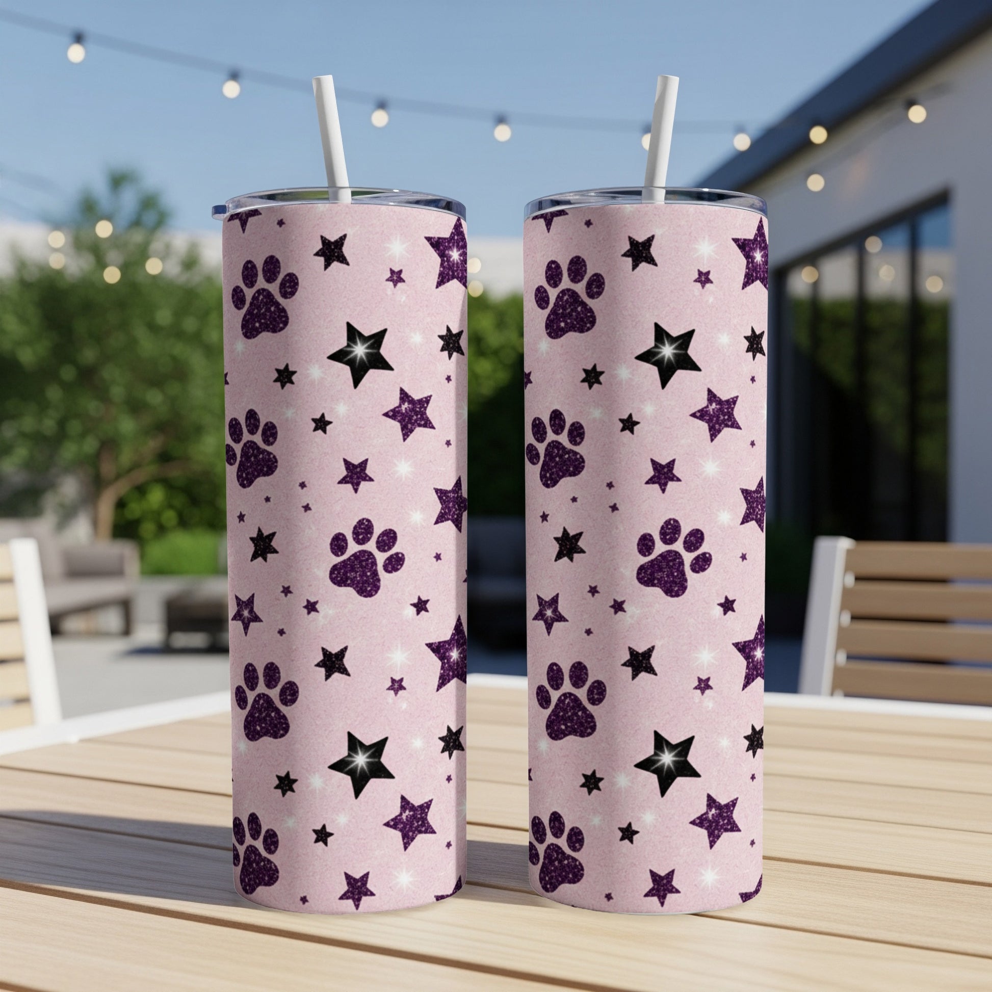 Two pink tumblers with paw print and star pattern on outdoor table.