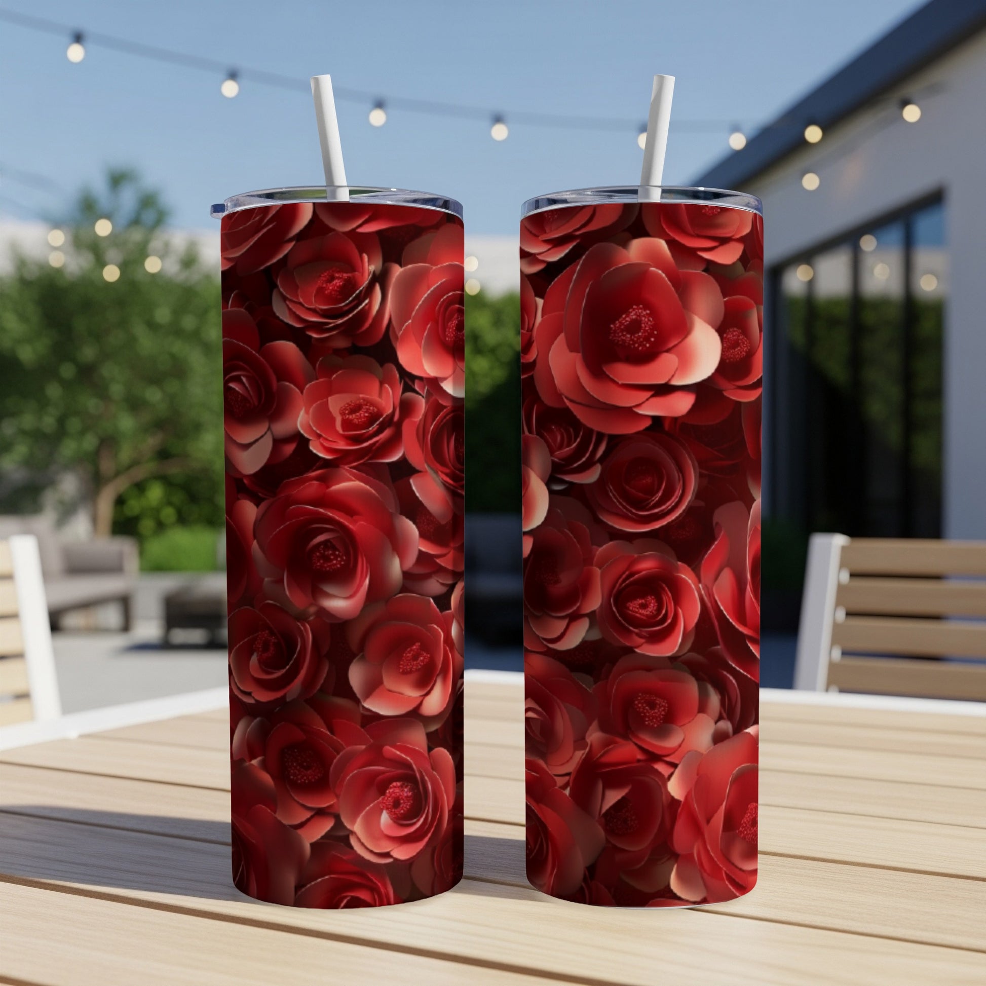 Two red rose pattern tumblers with straws on a wooden table outdoors.