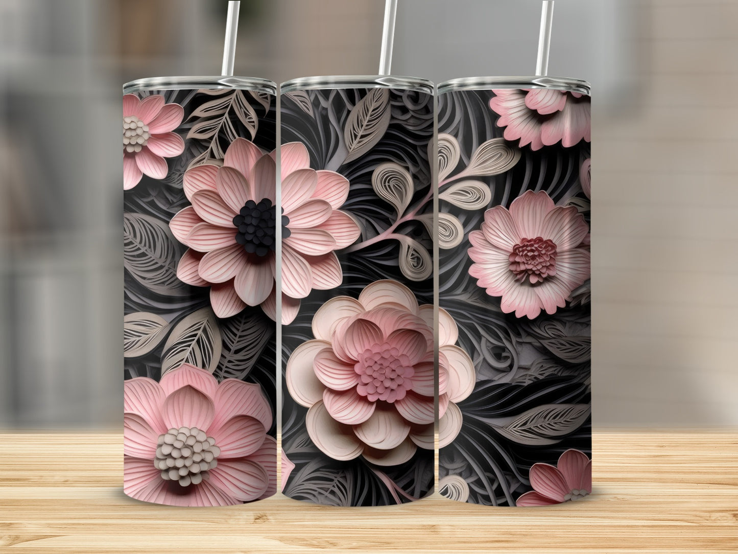 Three pink floral tumblers with straws on a wooden surface.