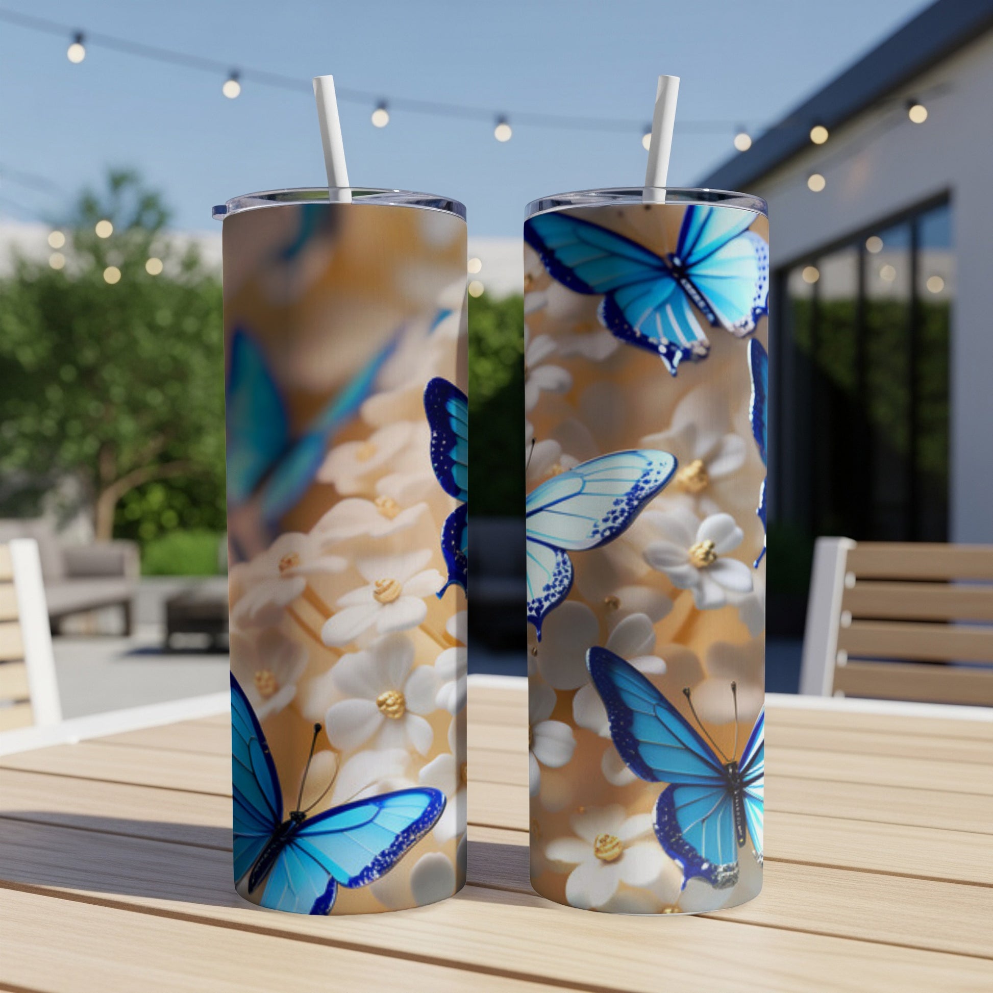 Two tumblers with blue butterflies and white flowers on a wooden table outdoors.