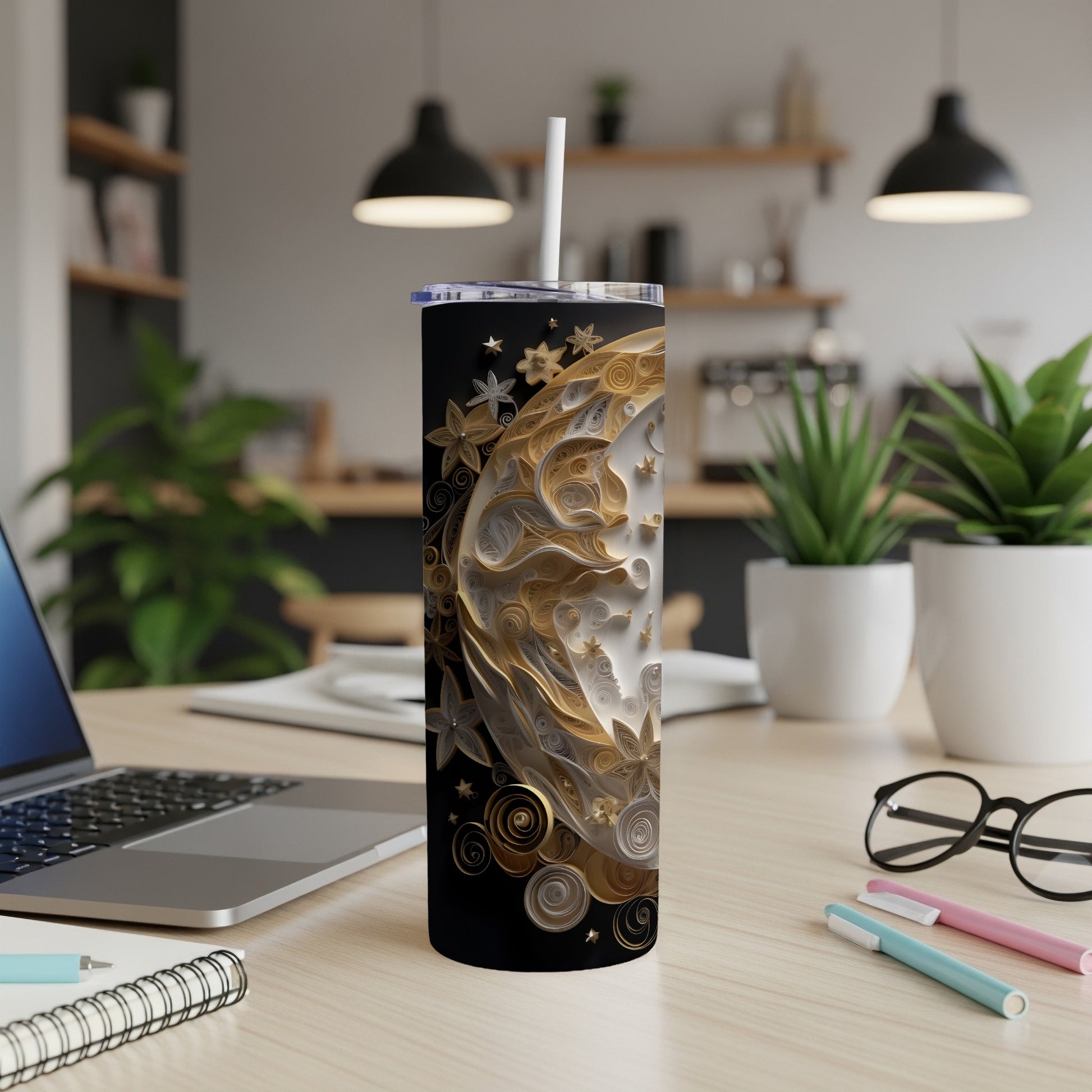 Black tumbler with crescent moon and floral design, straw, on a desk.
