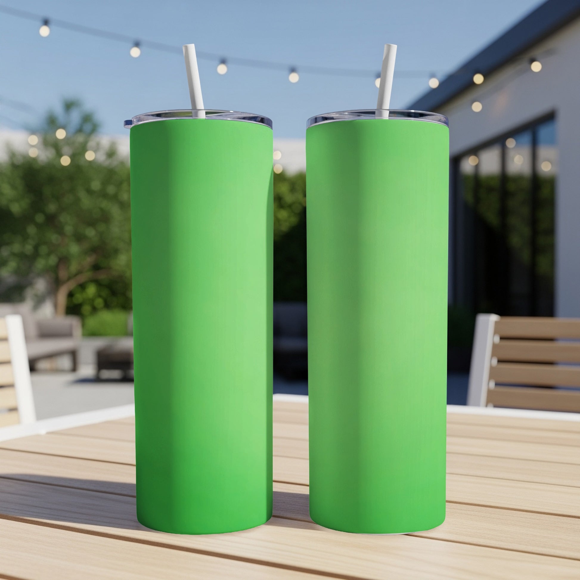 Two green tumblers with straws sit on a wooden table outdoors.