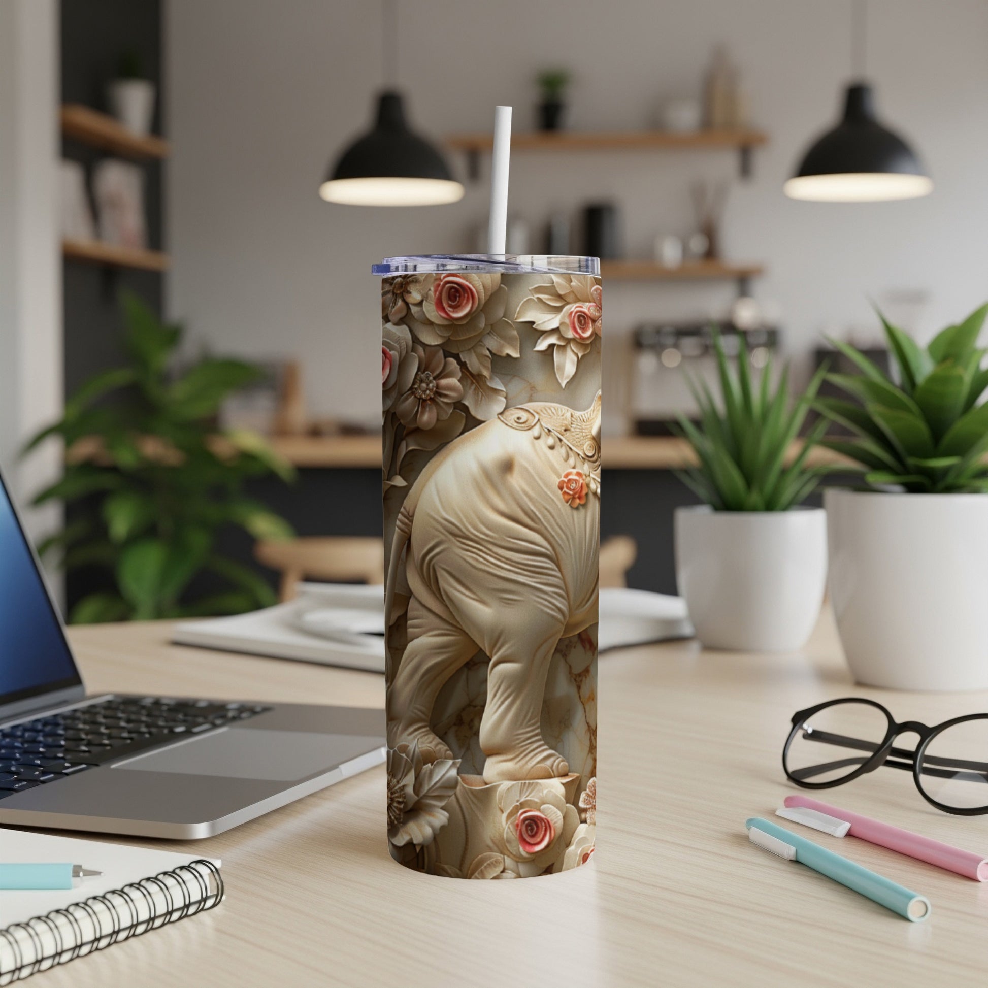 White elephant tumbler with floral embossed design and straw, on a desk.