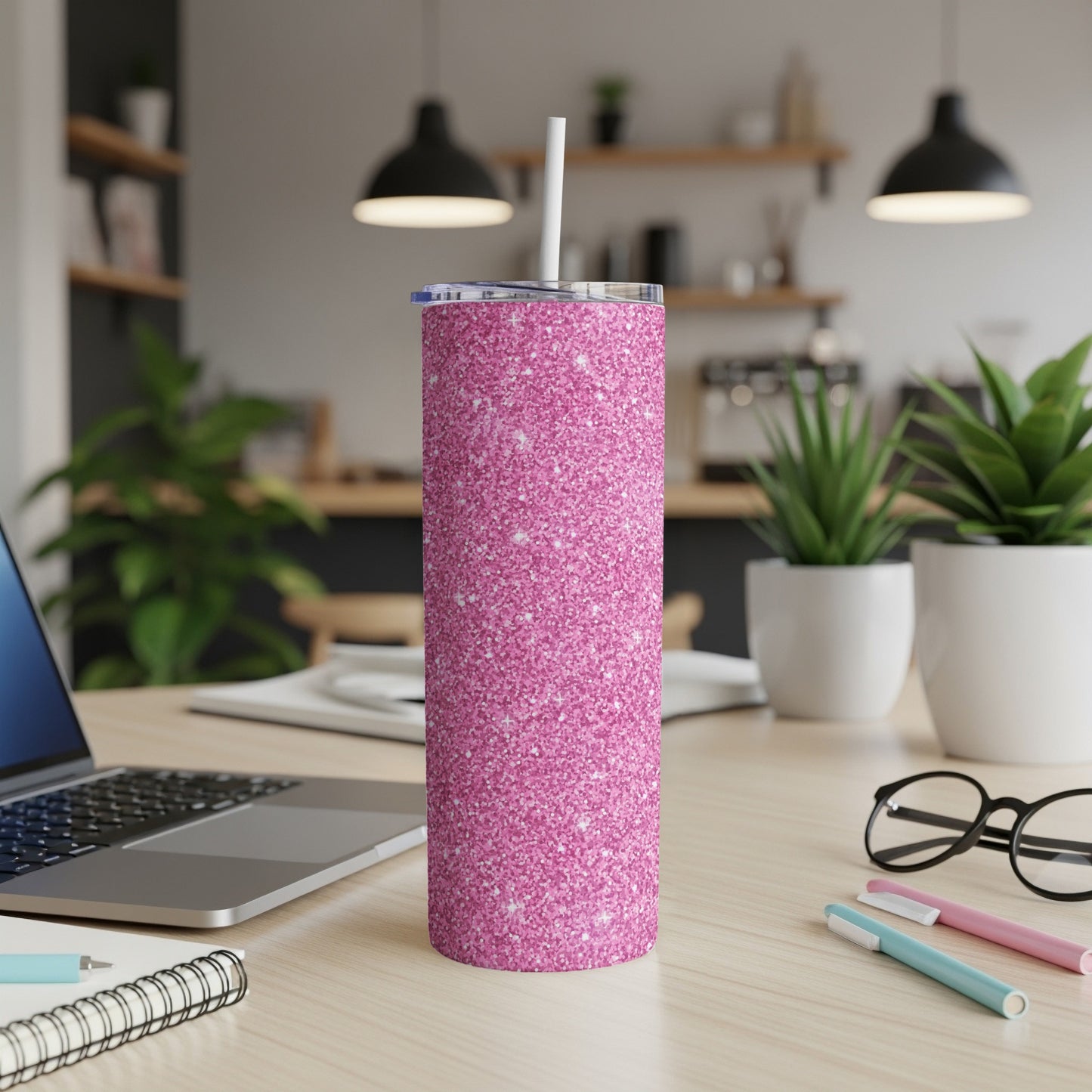 Pink glitter tumbler with straw on a desk with a laptop and pens.