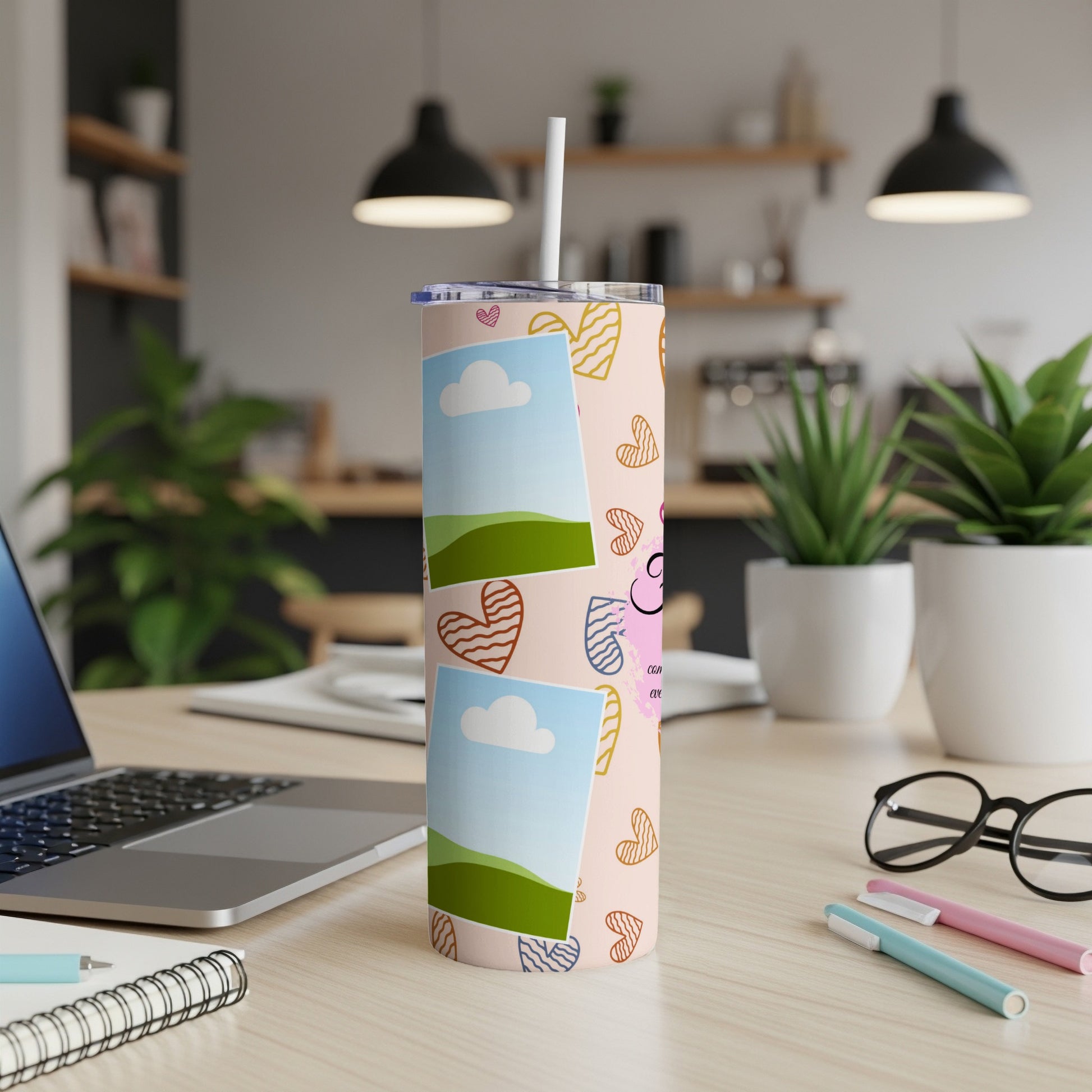 Pink tumbler with cartoon hearts, photo frames, and a straw on a desk.