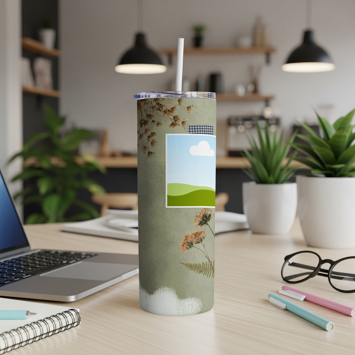 Green tumbler with dried flowers and a framed landscape image.