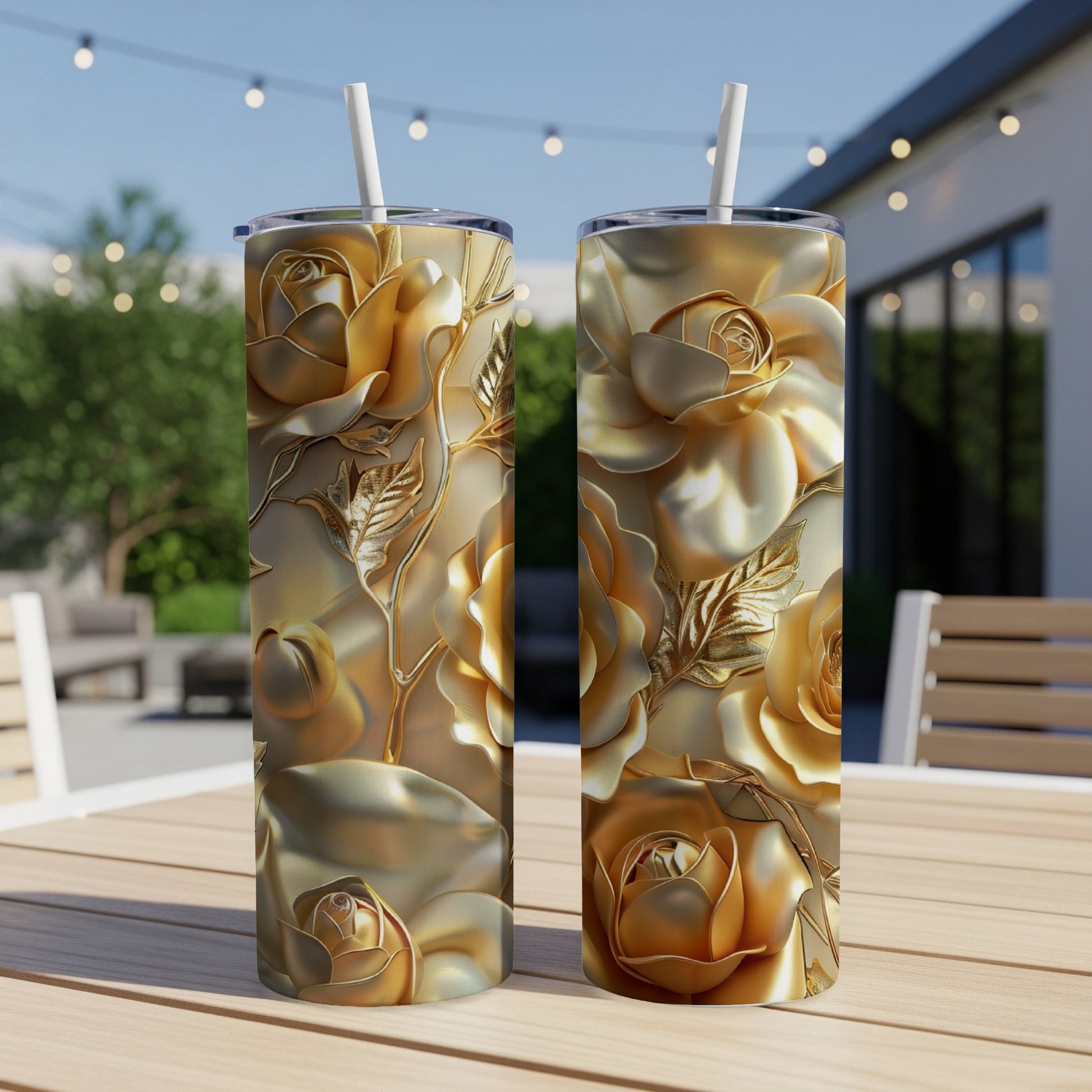 Two gold rose patterned tumblers with straws on a wooden table.