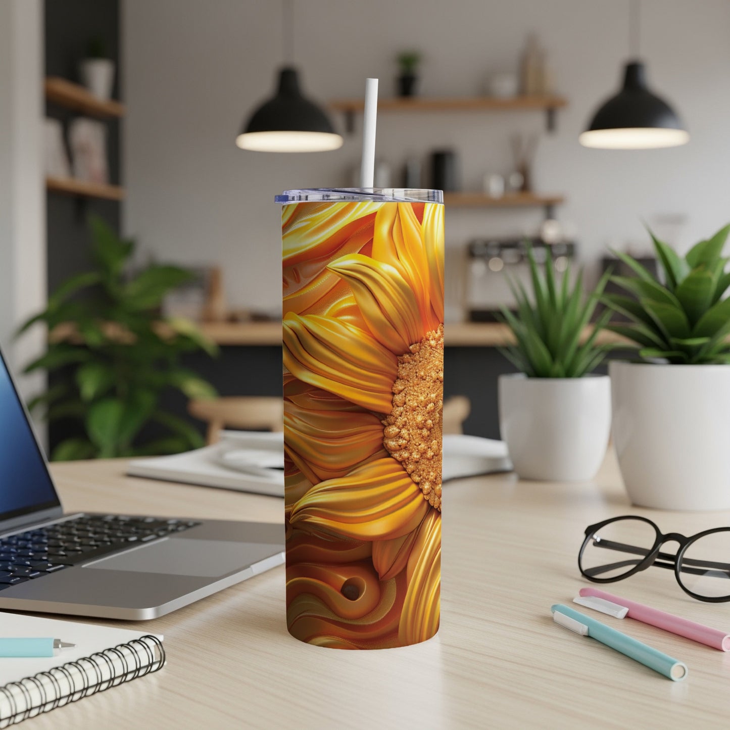 Sunflower tumbler with straw on a desk with laptop and pens.